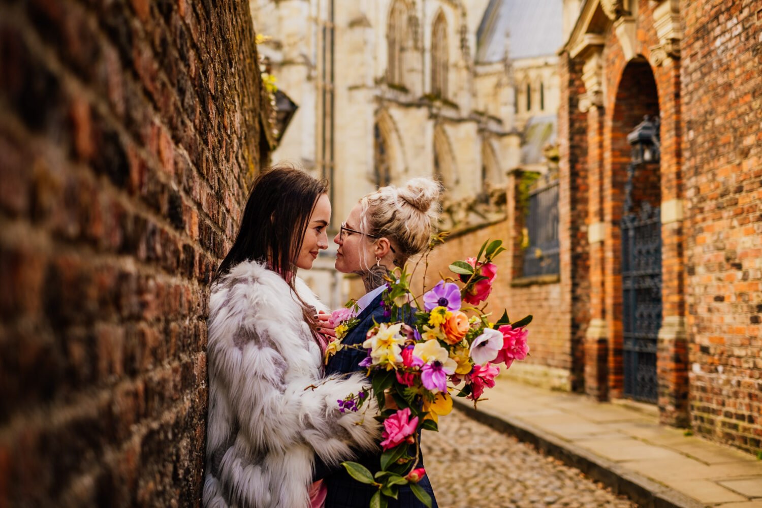 bride in fur coat looking at bride with bright flowers in york