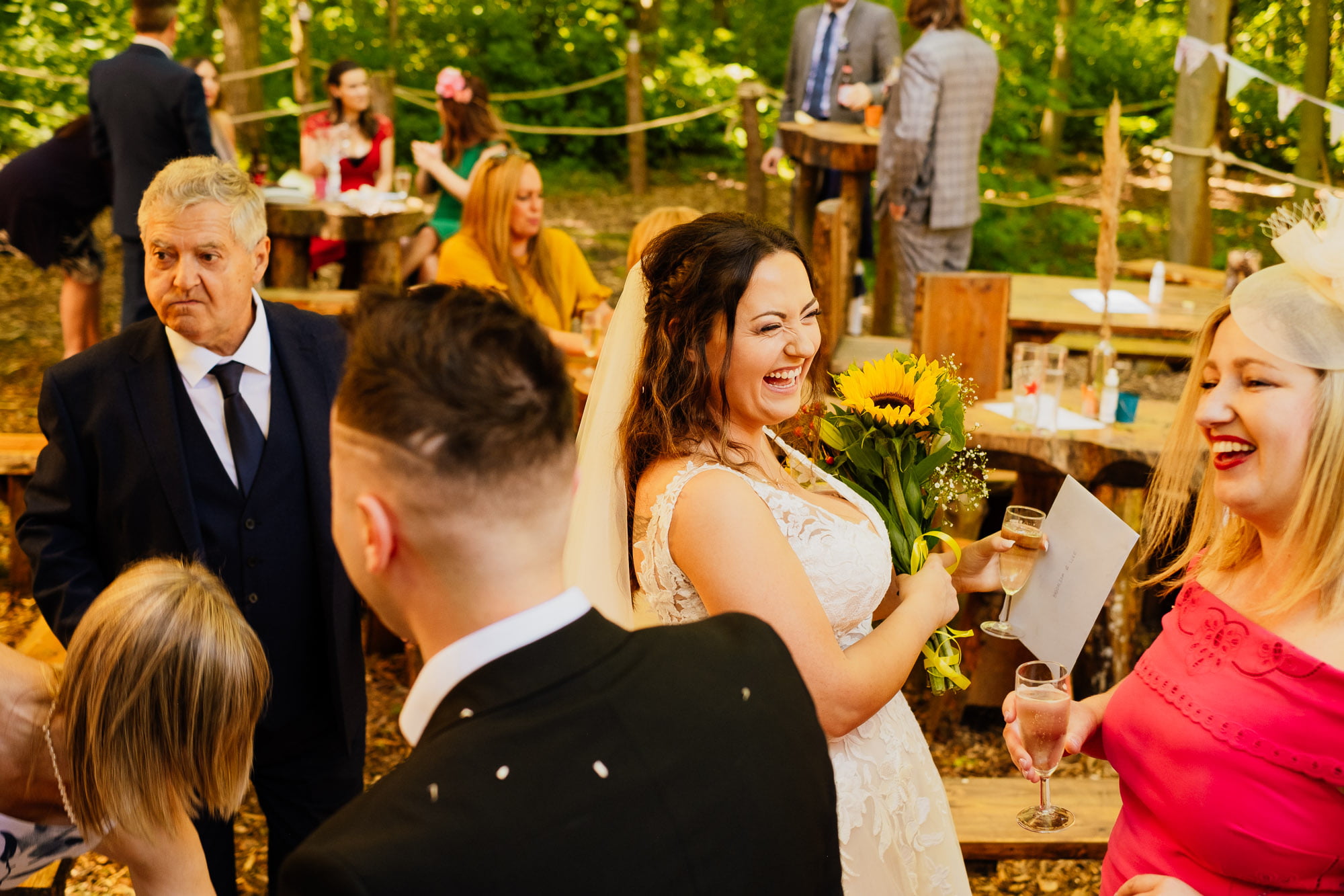 Bride holding sunflowers laughing with guests