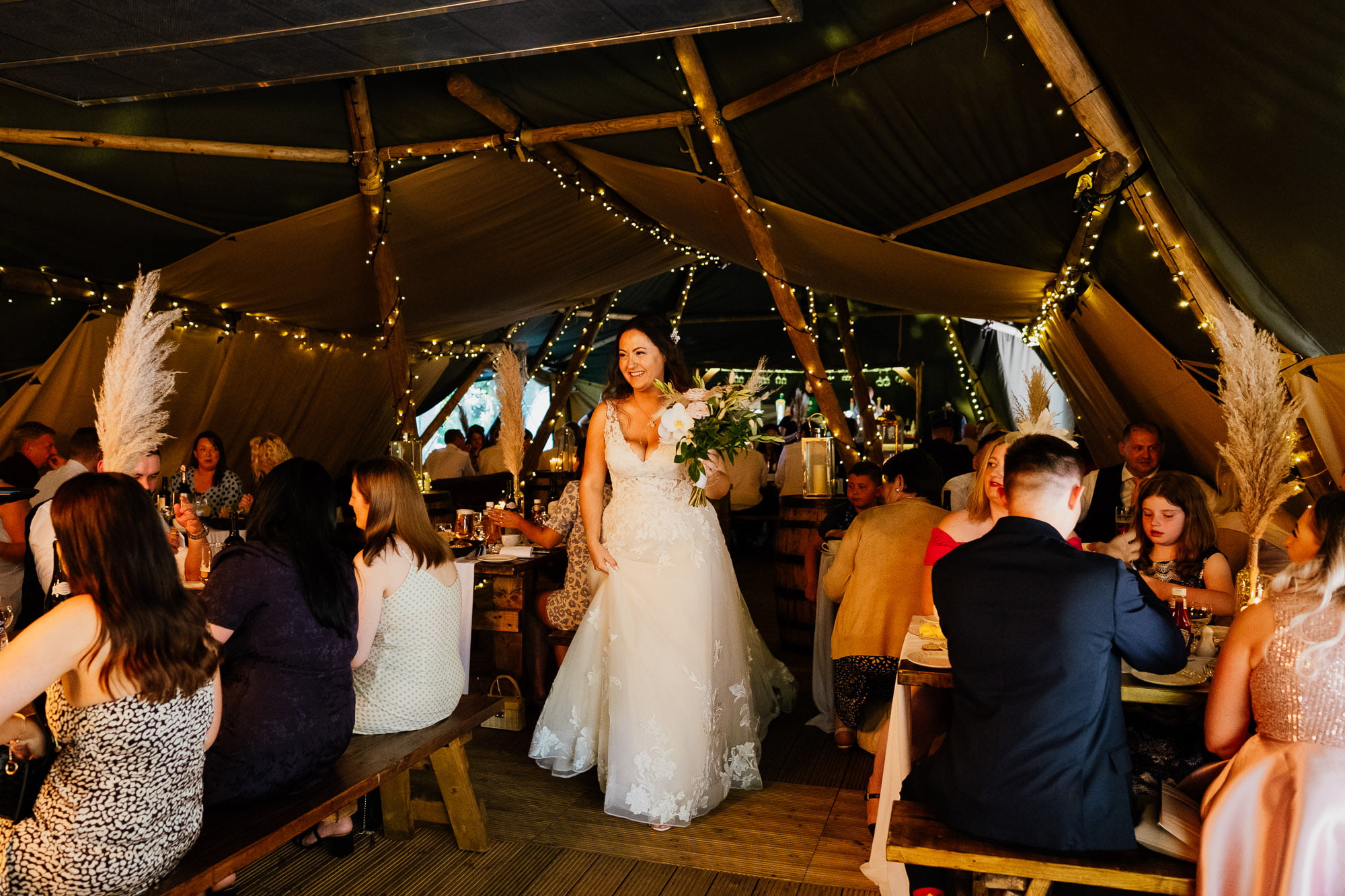 Bride walking through tipi with guests sat ready to eat