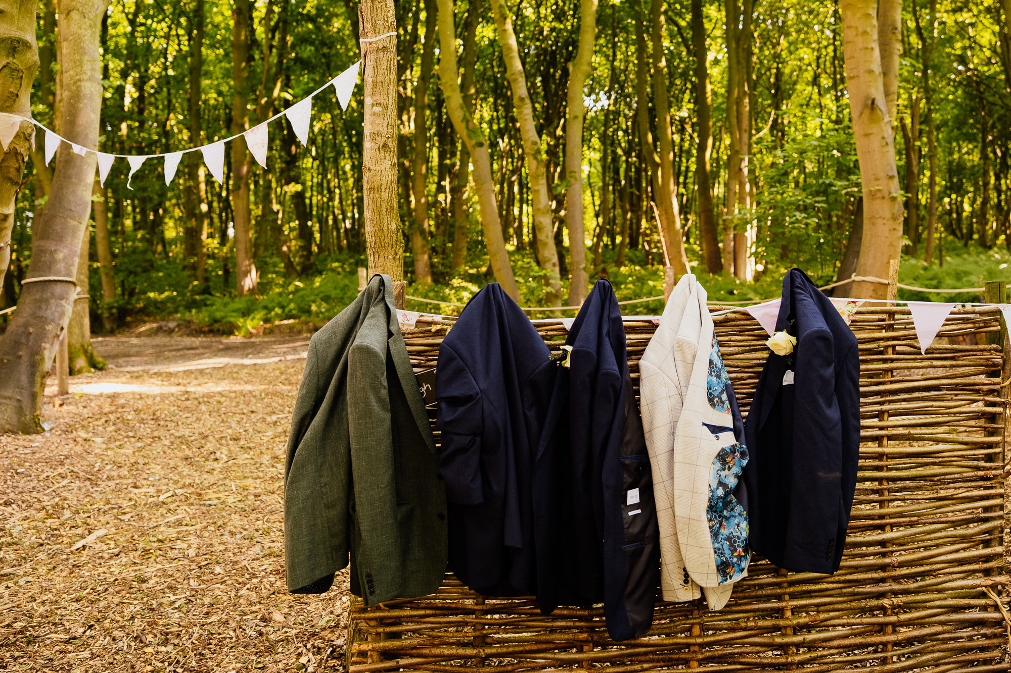 Five jackets hung on wicker fence in woodland