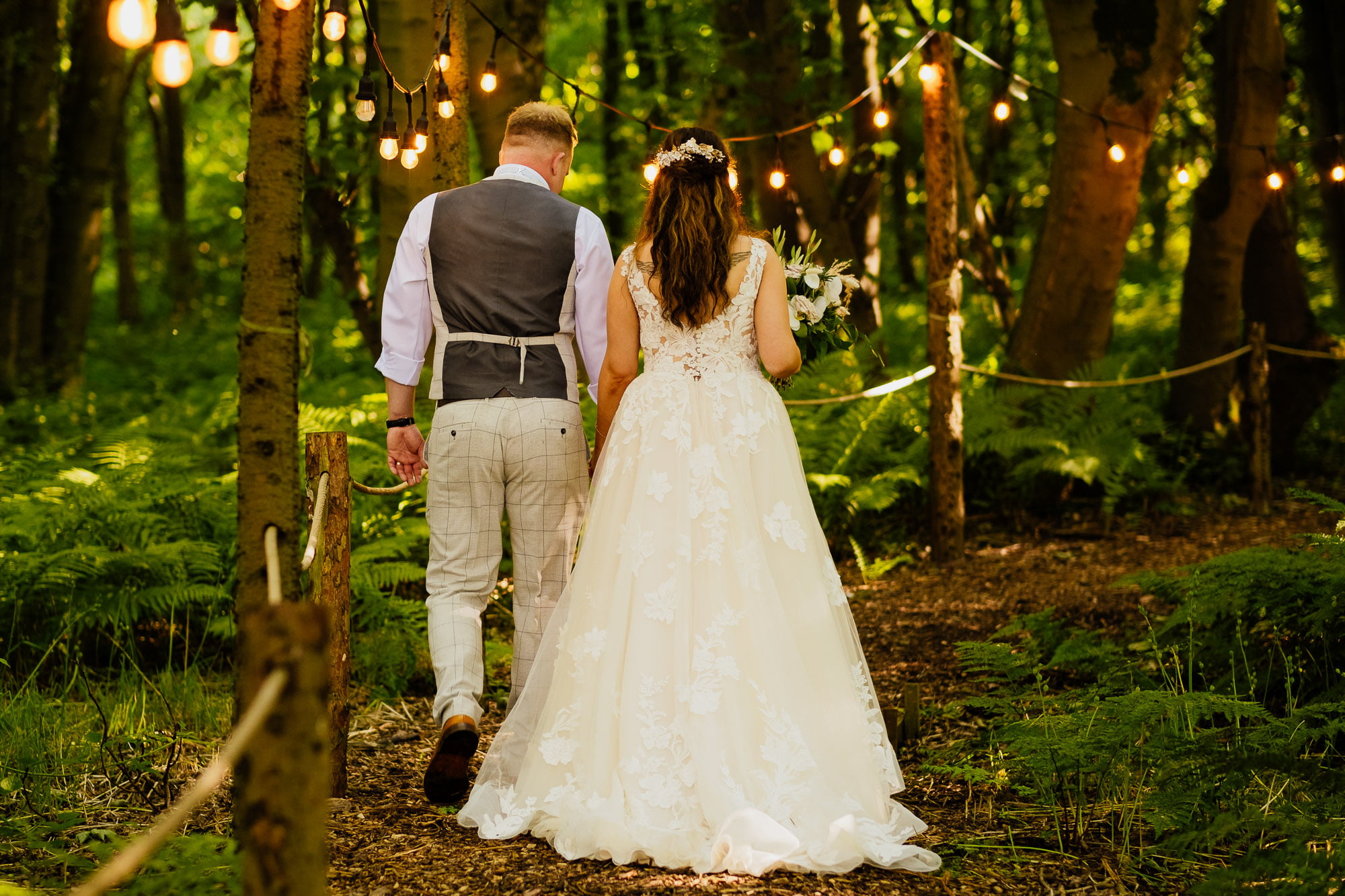 bride and groom walking away with festoon lighting at cockley wood outdoor wedding