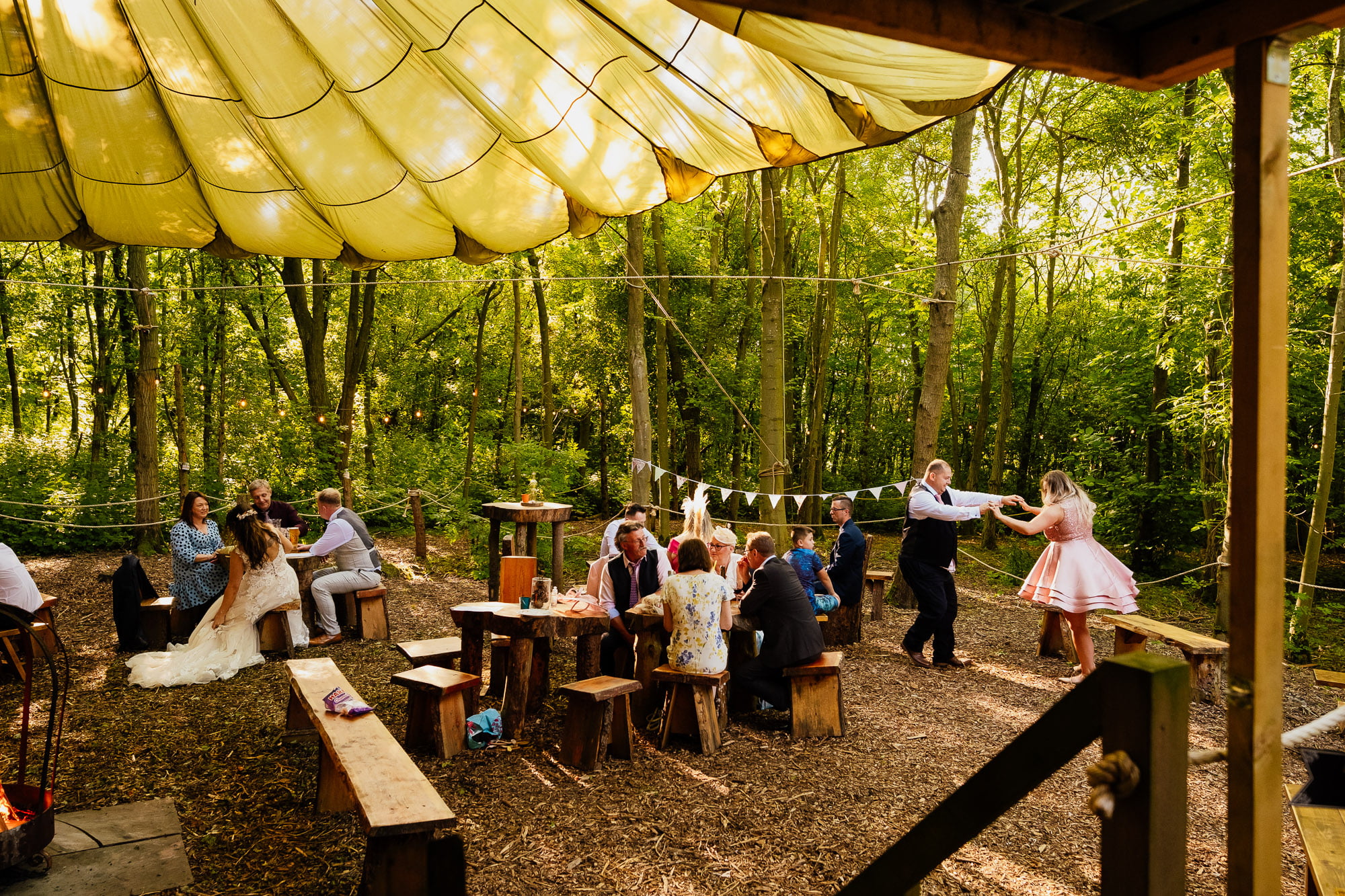 wedding guests dancing whilst other sit and chat in woodland area