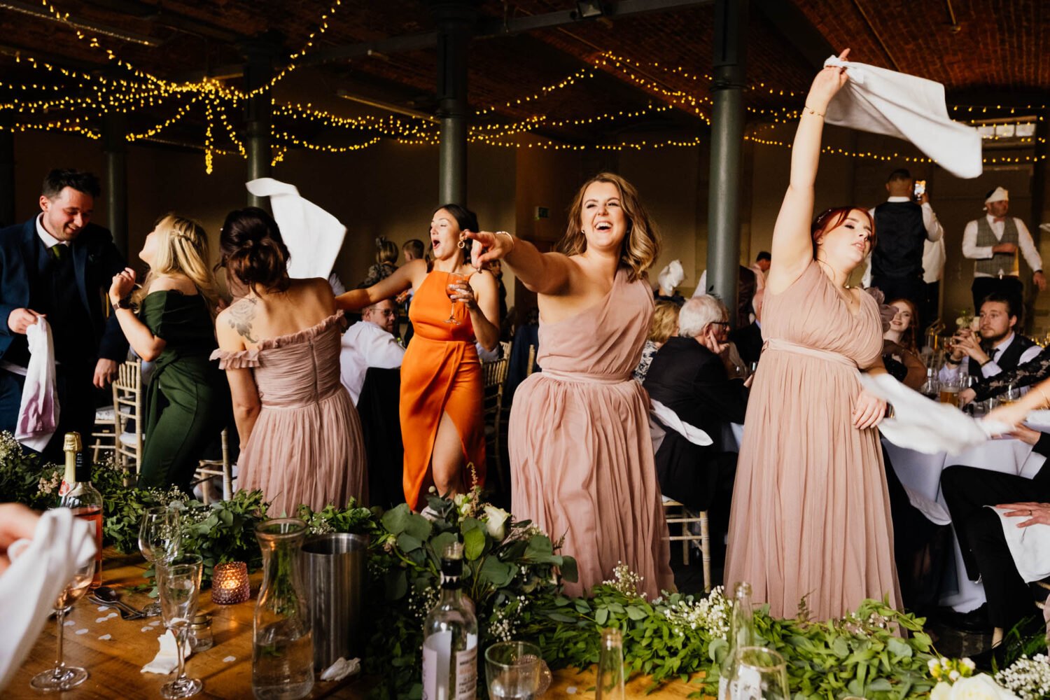 Wedding guests pointing and waving napkins around during wedding breakfast.