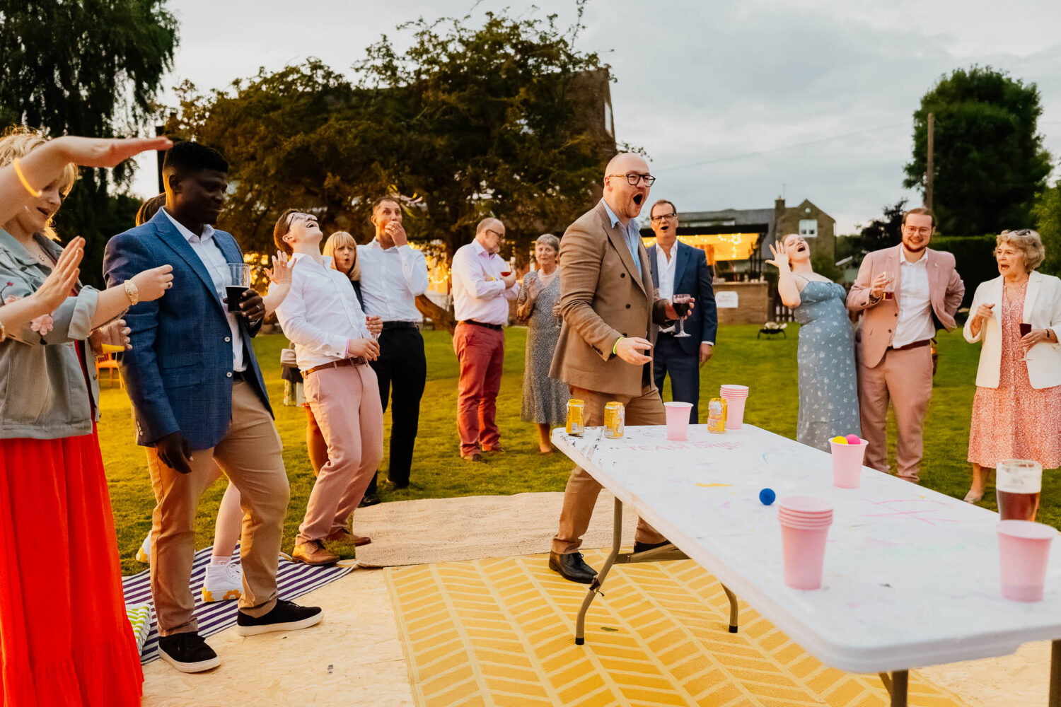 A large group of wedding guests playing beer pong outside in a garden in summer