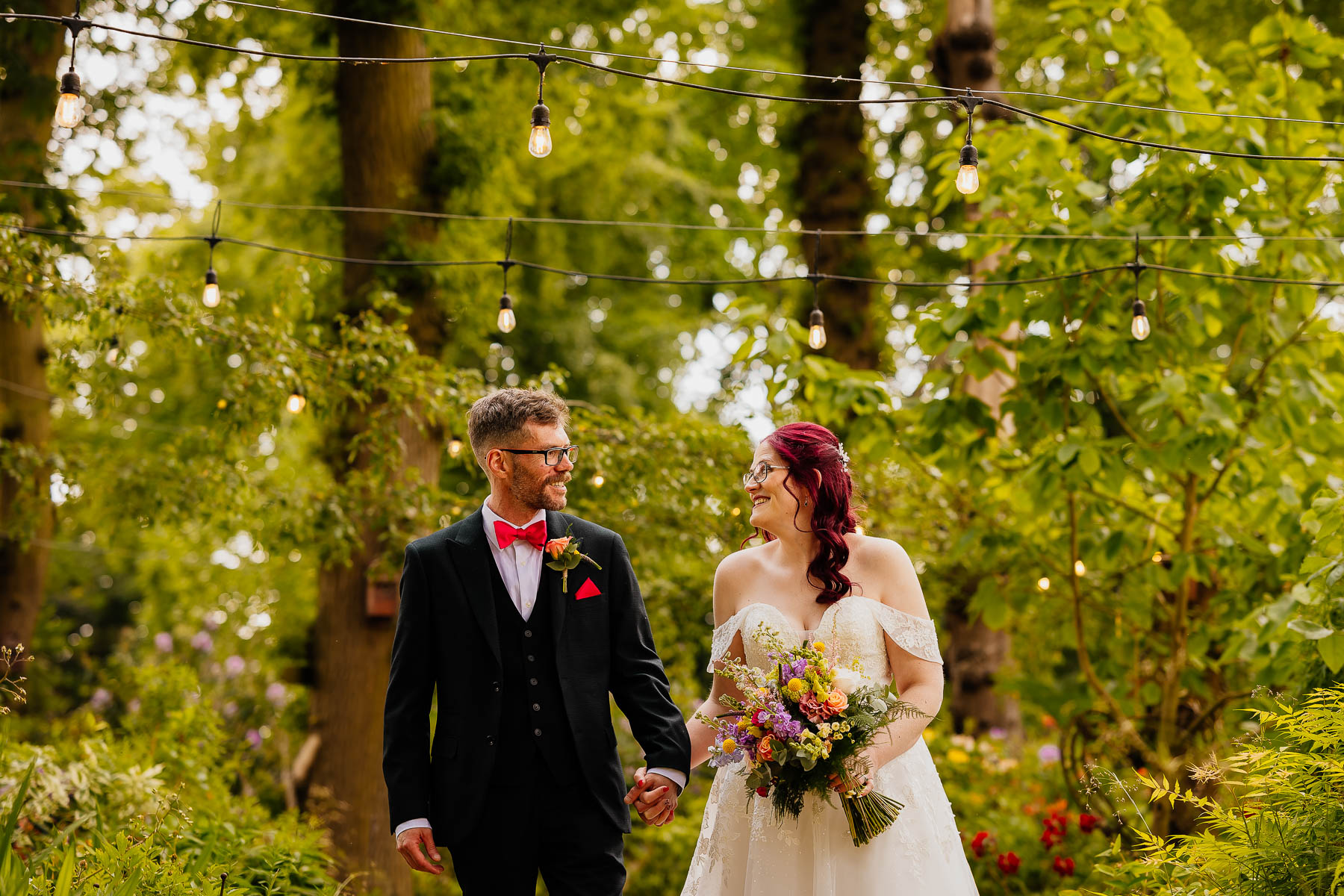 Bride and groom walking through woodland with festoon lights