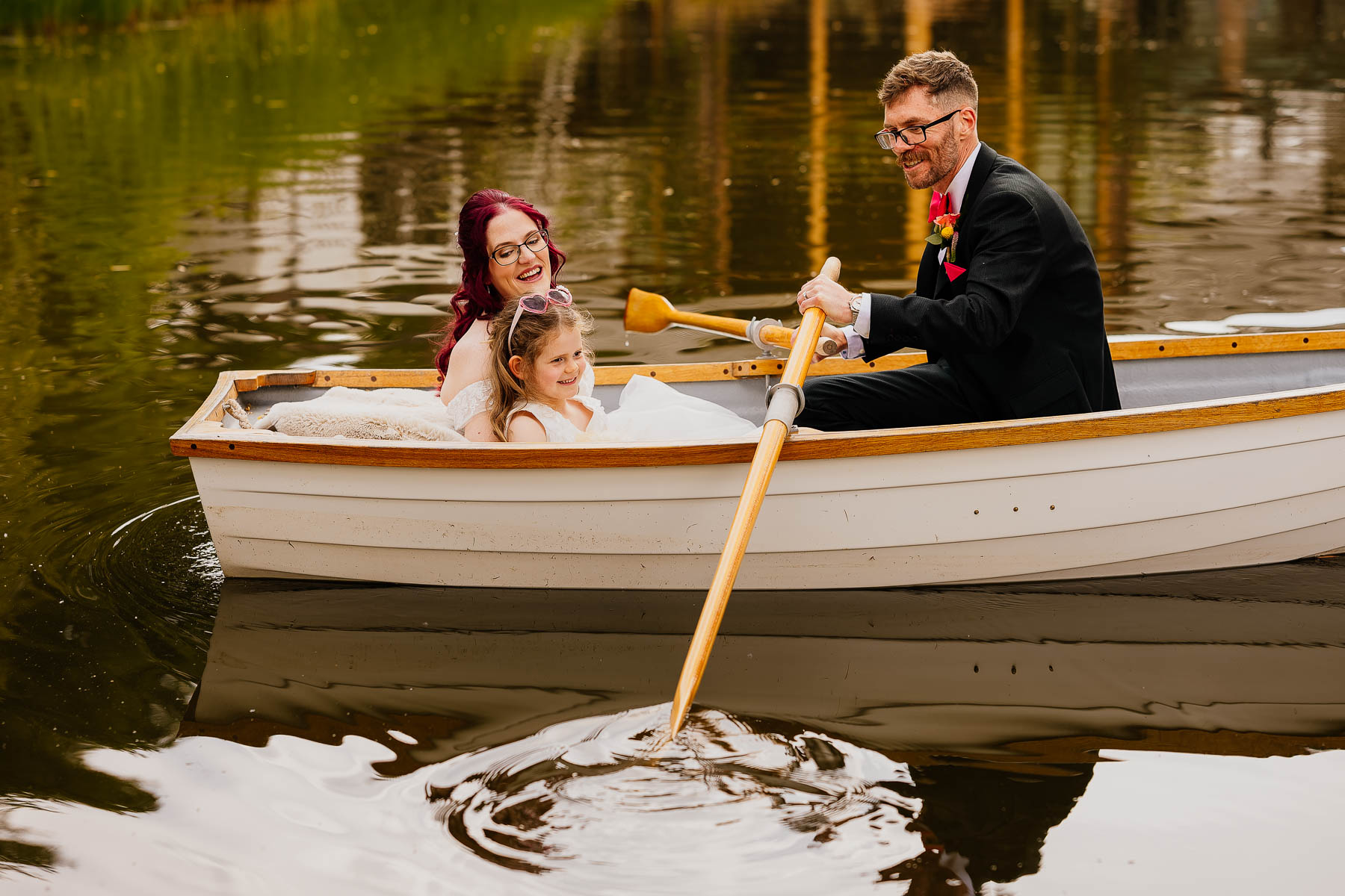 Bride and daughter in boat with groom rowing