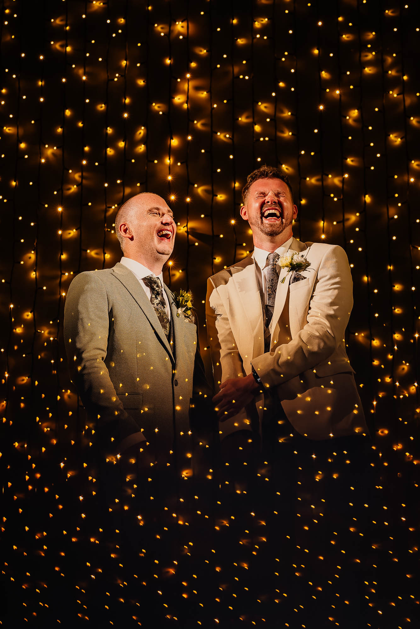 grooms laughing during ceremony surrounded by fairy lights