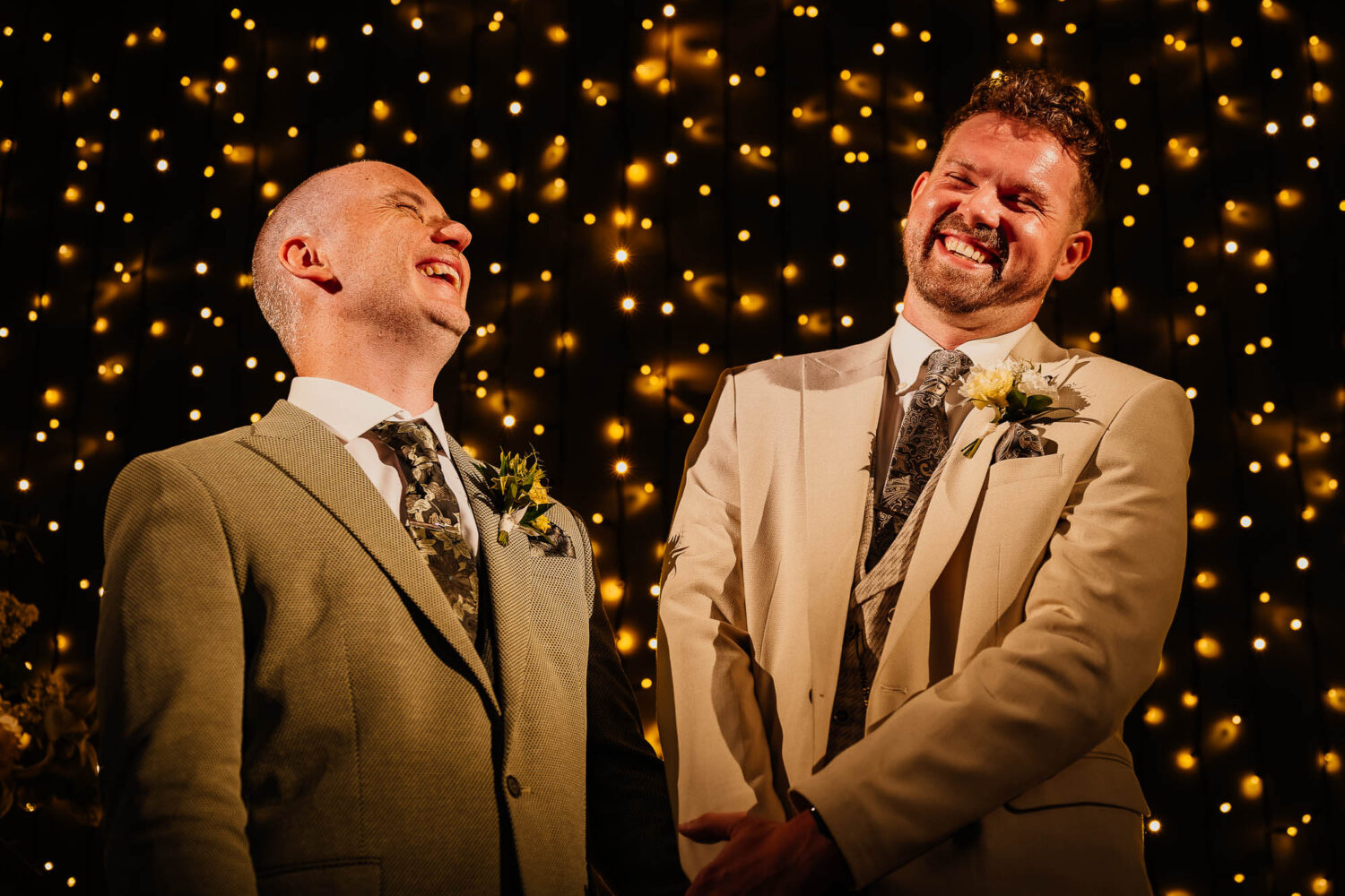 Grooms laughing during Wharfedale Grange ceremony with fairy light backdrop