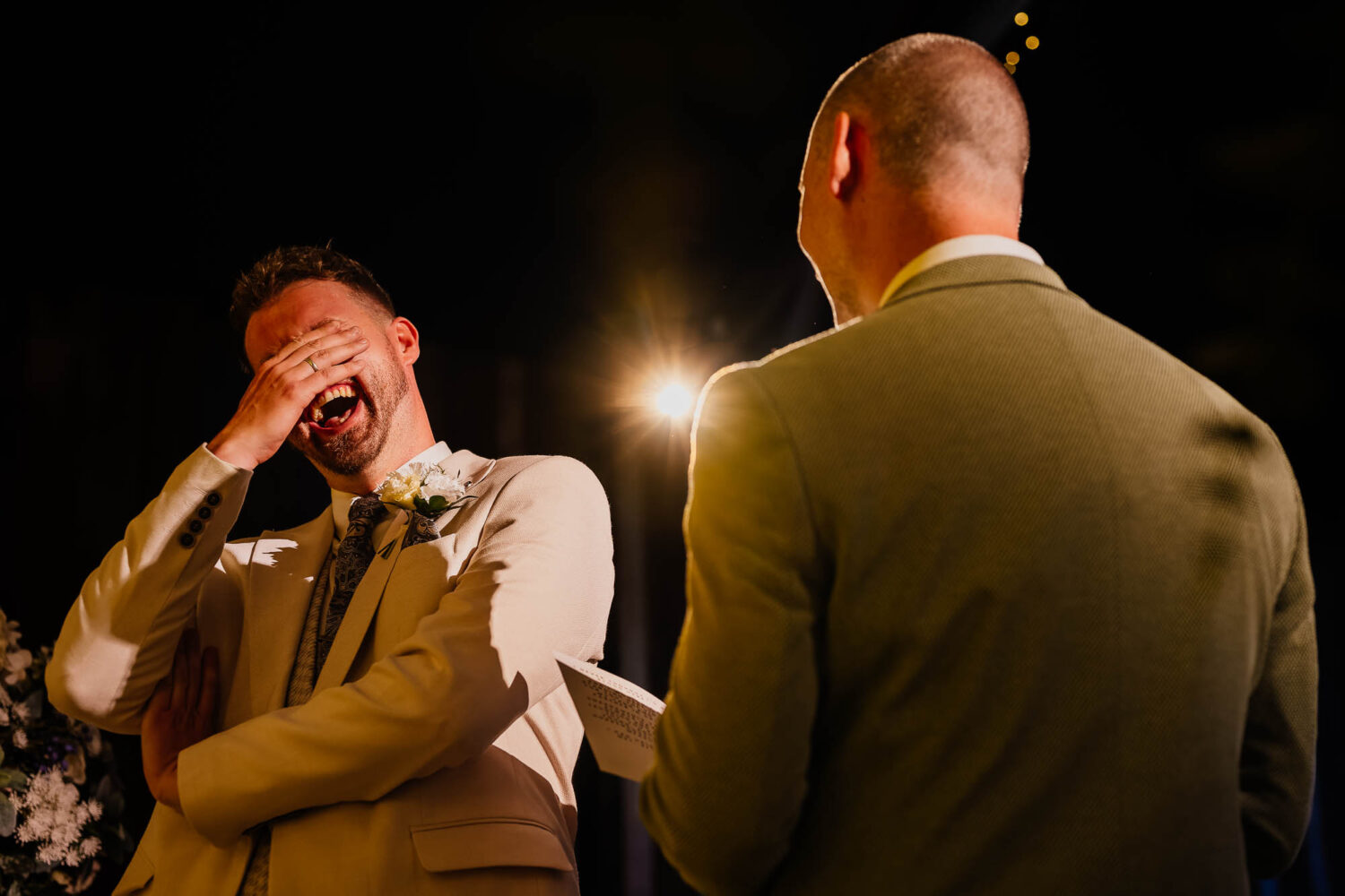 Groom laughing with his hand over his face during wedding vows