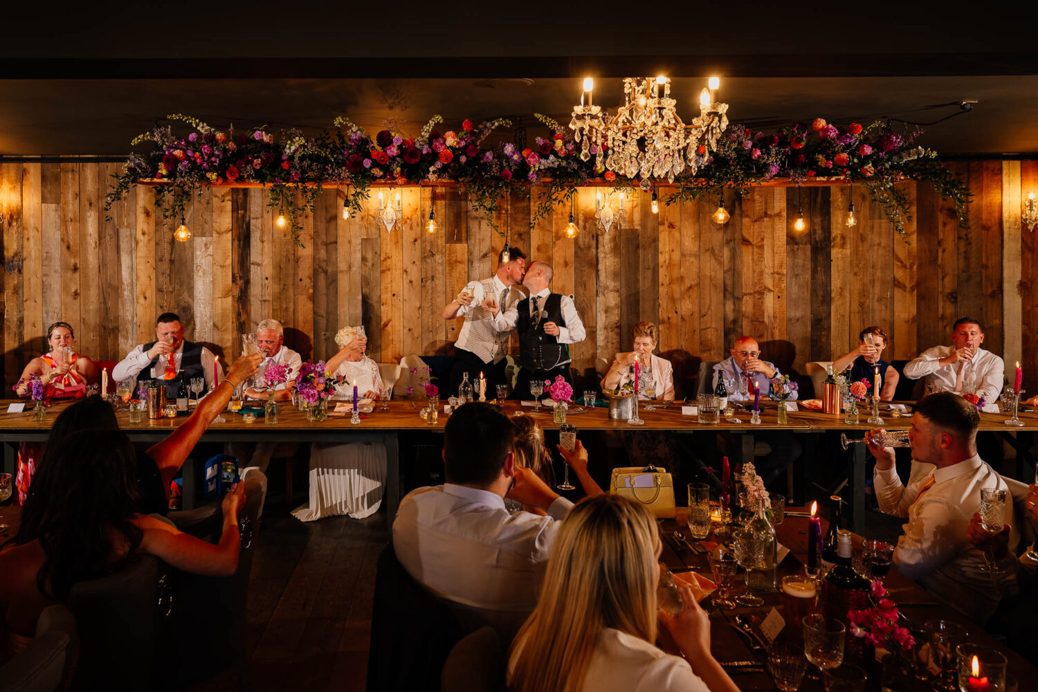 Grooms kissing on top table at Wharfedale Grange wedding with everyone around cheering