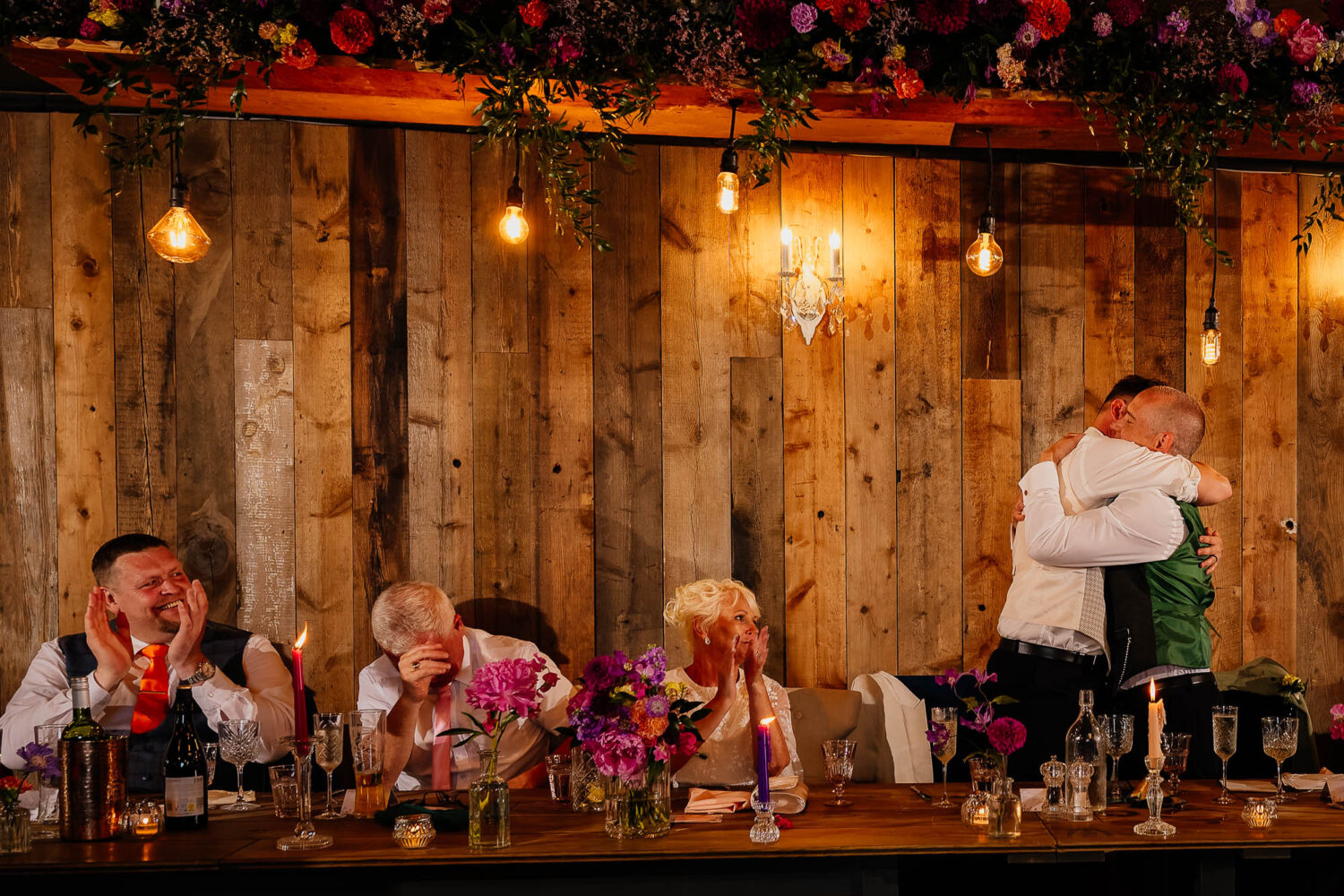 Grooms hugging with reactions from guests next to them