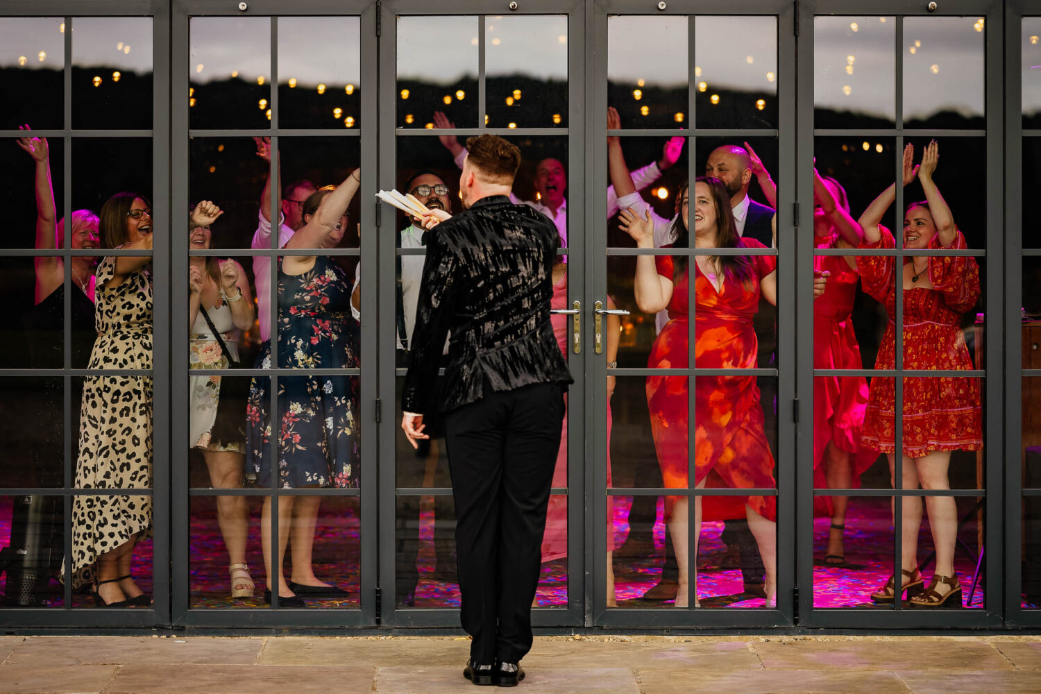 Guests dancing at Wharfedale Grange with groom watching through the window