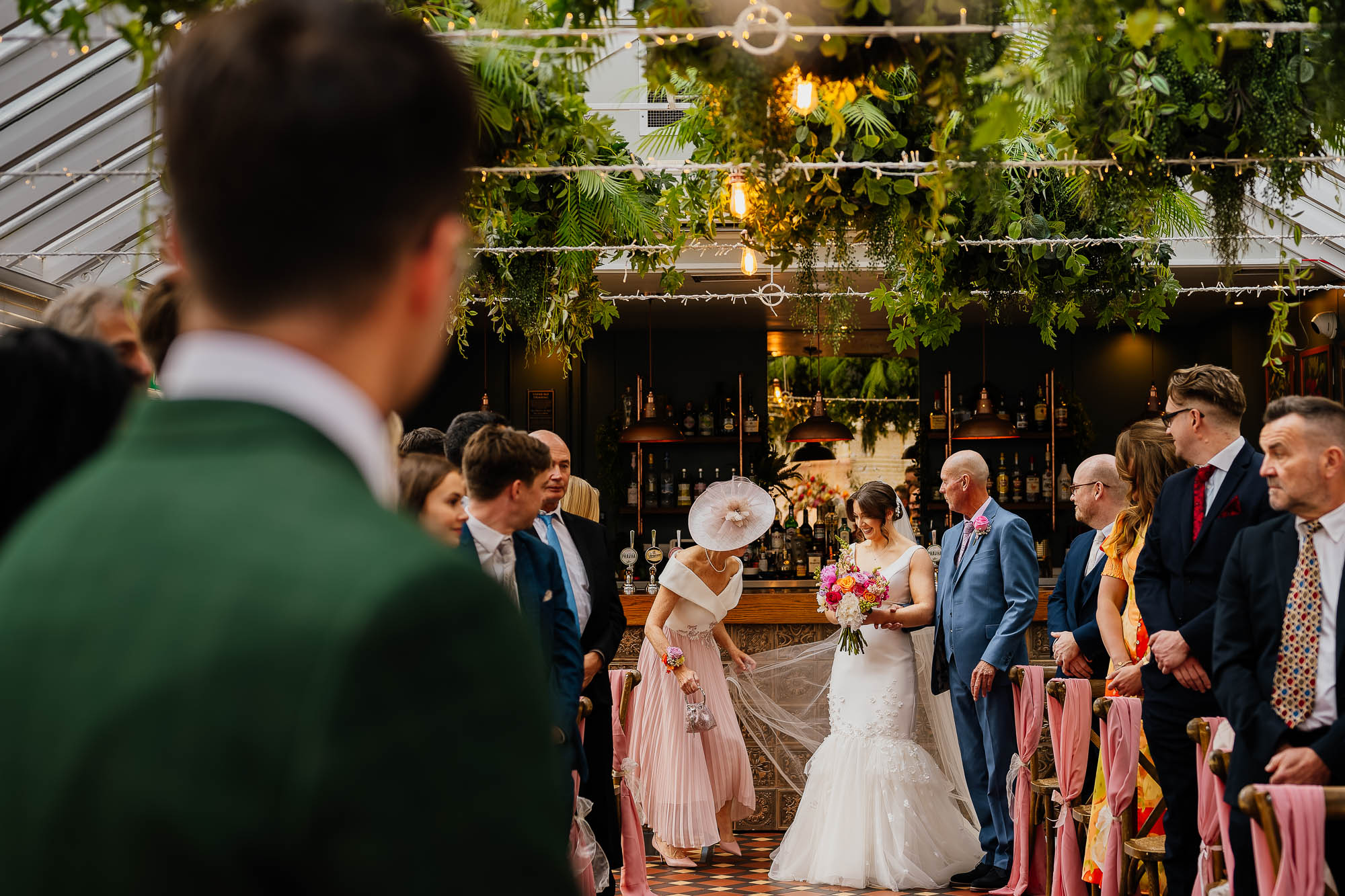Bride at the end of the aisle with mum holding veil and groom watching