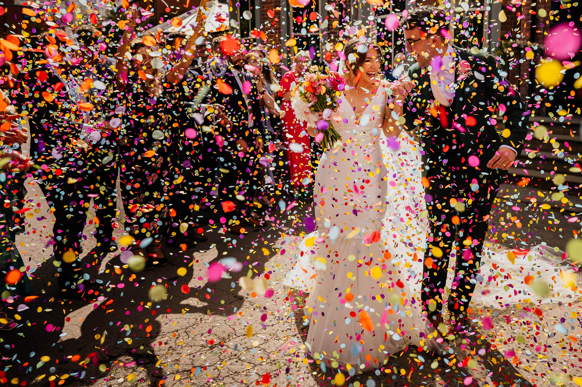 Bride and groom holding hands showered in colourful paper confetti