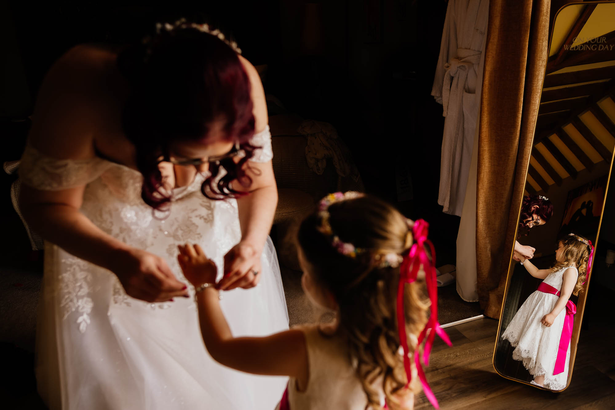 Bride putting bracelet on daughter reflected in the mirror