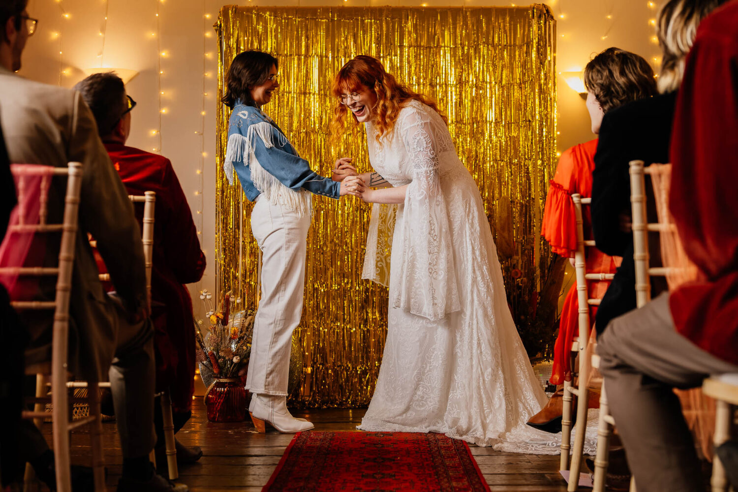 Couple holding hands laughing with gold foil backdrop during ceremony