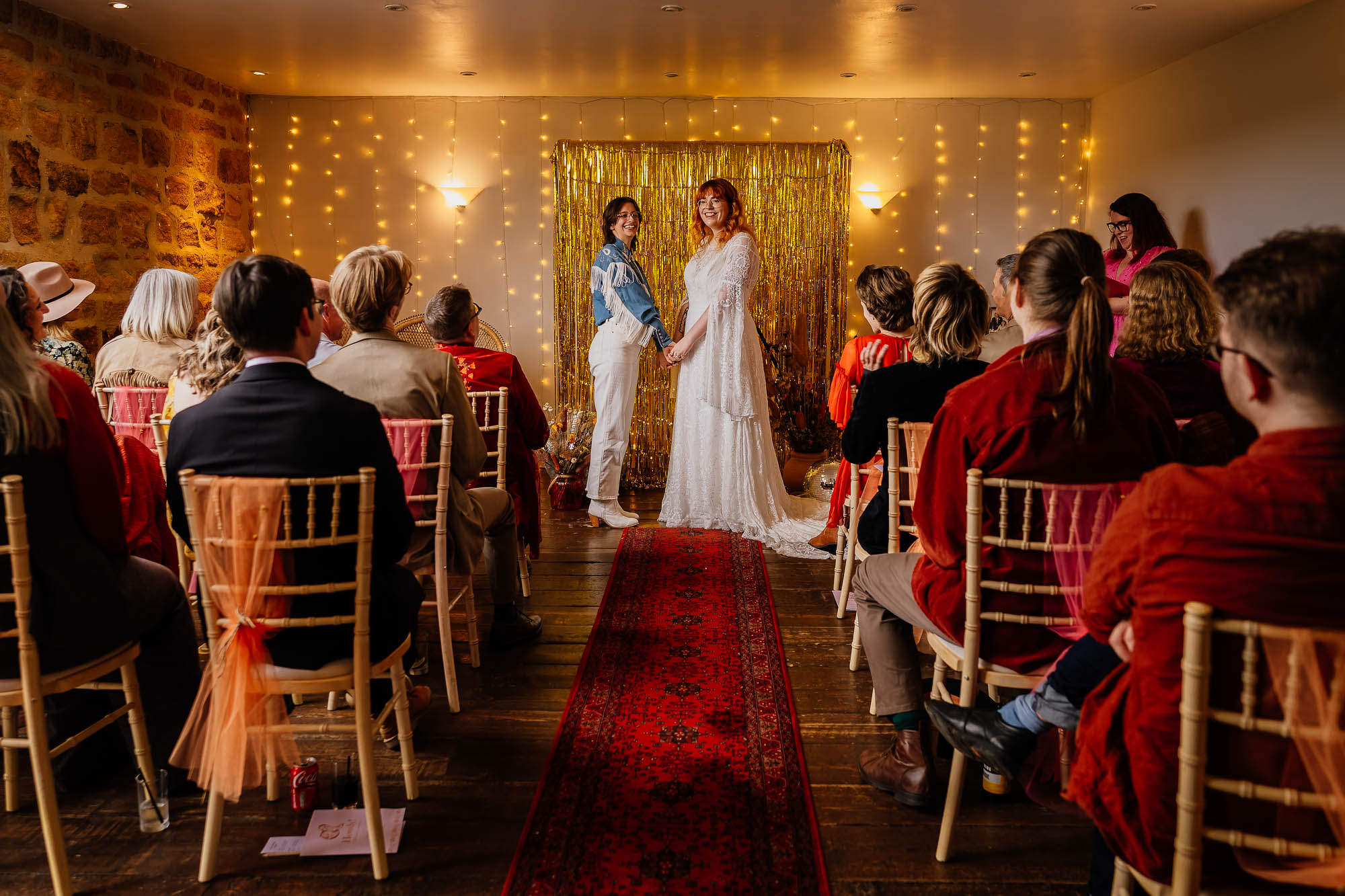 Guests holding hands in front of gold streamer backdrop during wedding ceremony