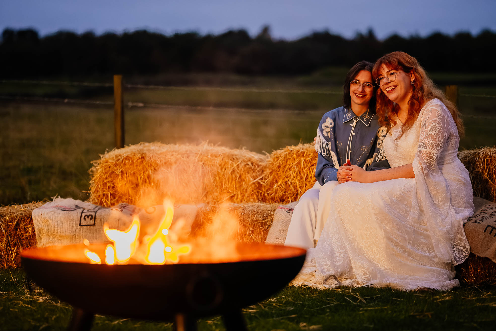 Couple sat on hay bales next to a firepit in the evening