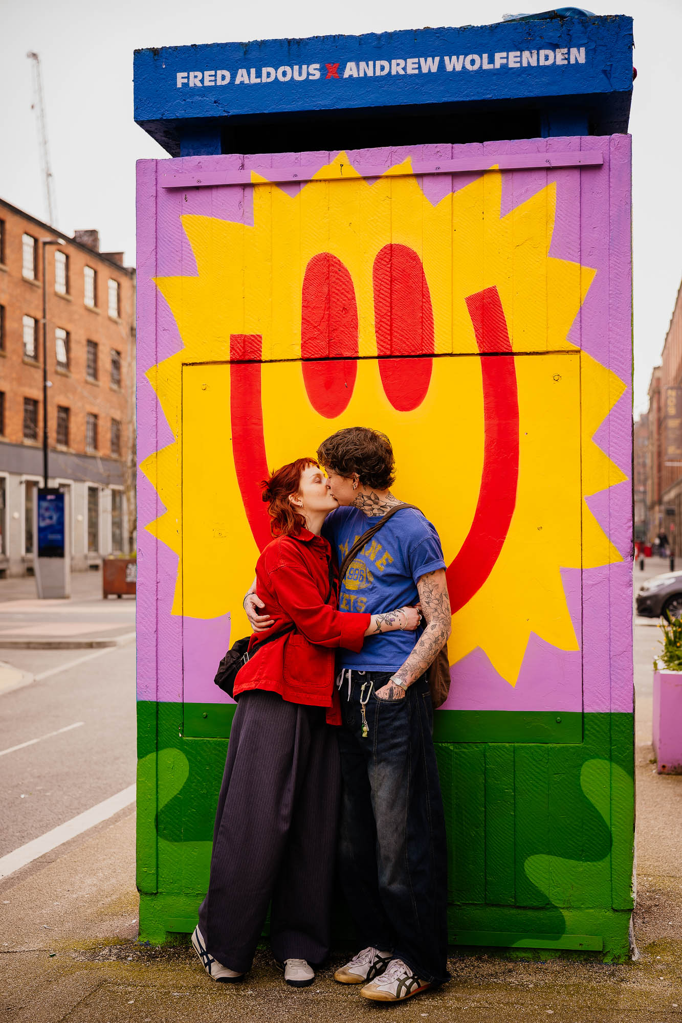 Couple kissing under Andrew Wolfenden mural in Manchester