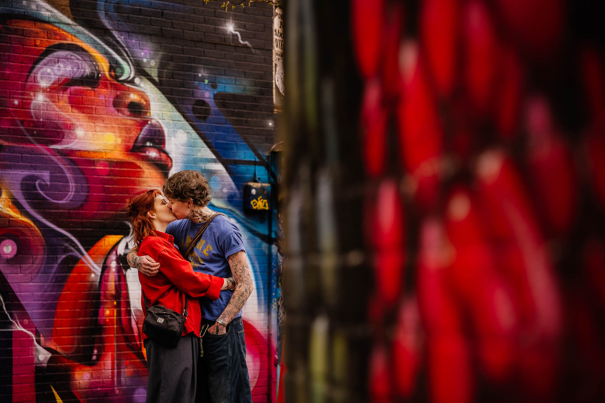 Couple kissing in front of red painted mural street art