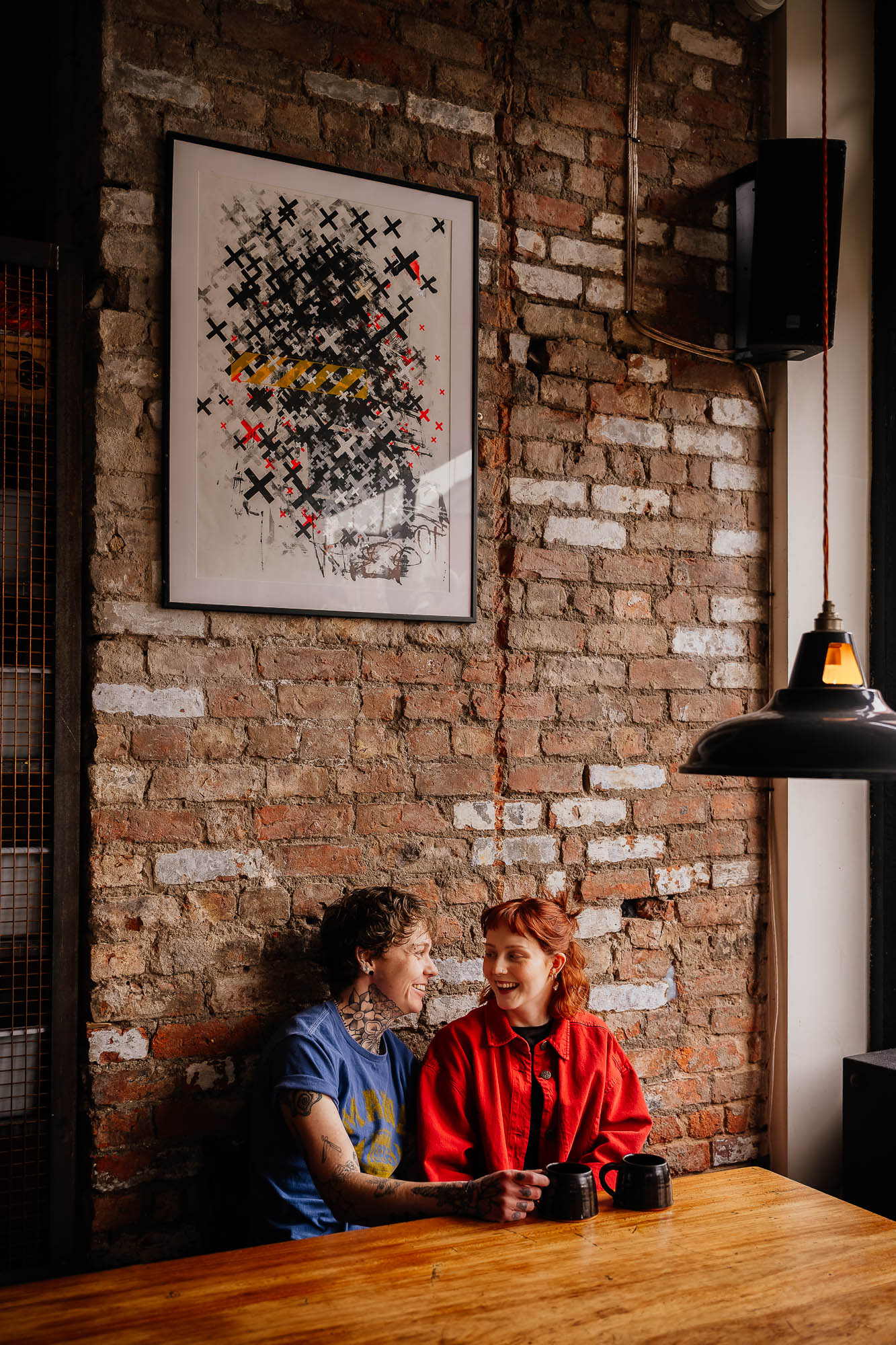 Couple laughing drinking coffee in Mackie Mayor against brick wall