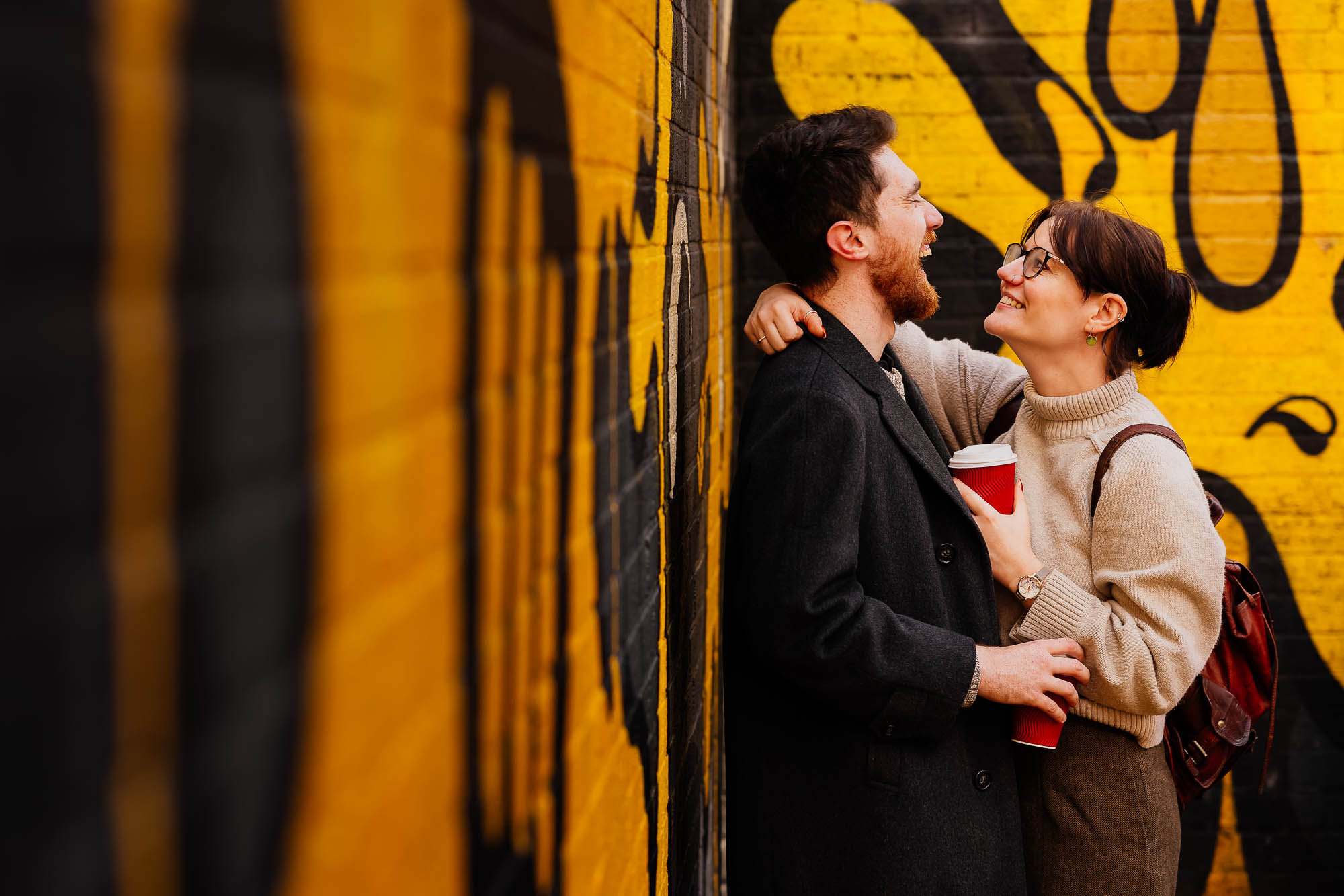 Couple laughing leaning on yellow and black mural