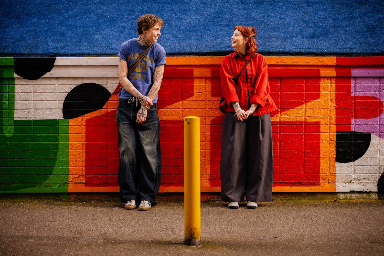 Couple standing smiling at each other leaning on Fred Aldous backdrop