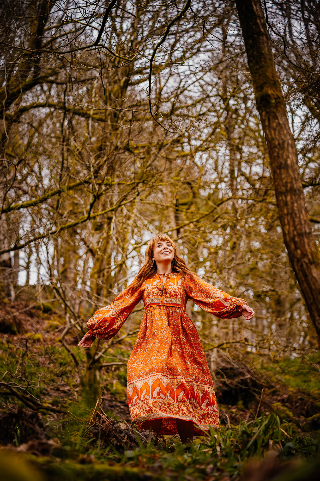 Woman in orange dress dancing in woodland area