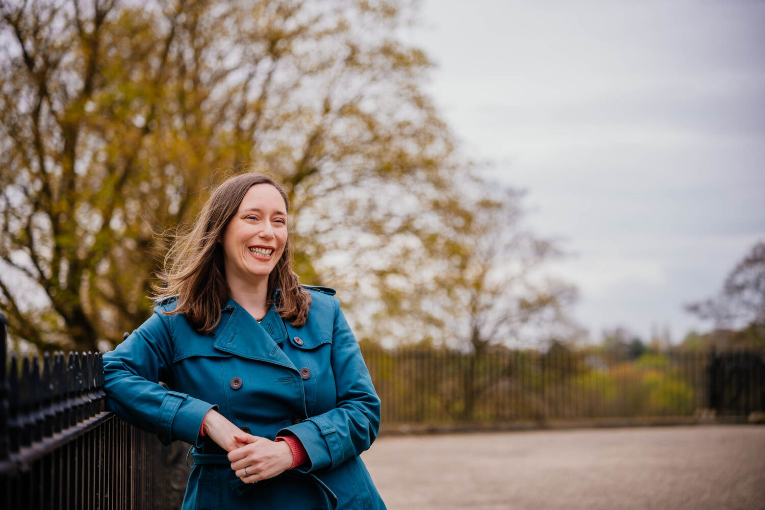 Woman in blue coat smiling leaning on metal railings