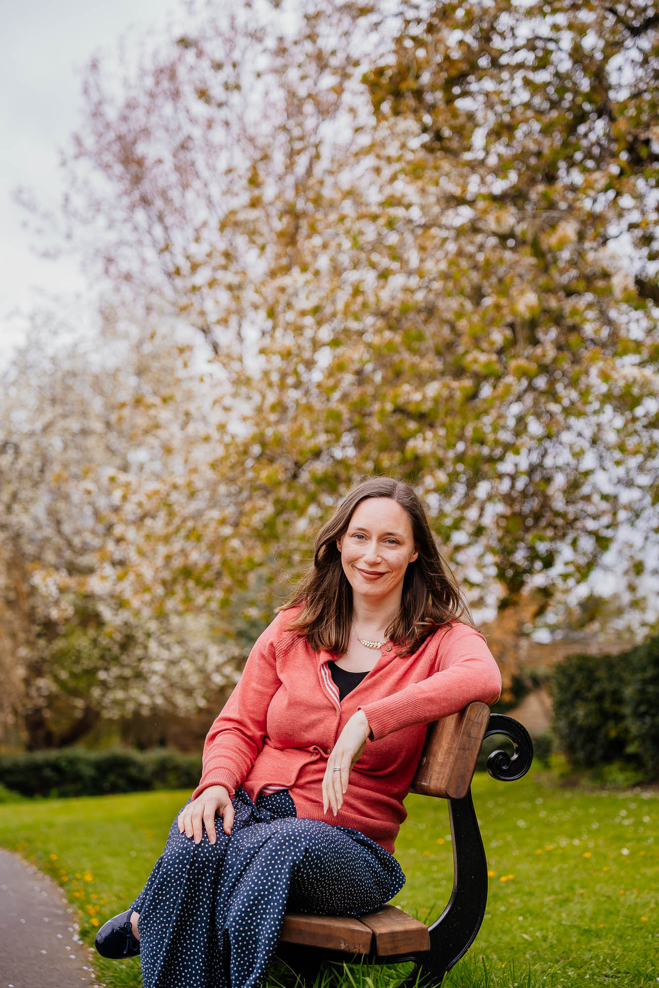 Woman sat on bench smiling with white blossom tree backdrop