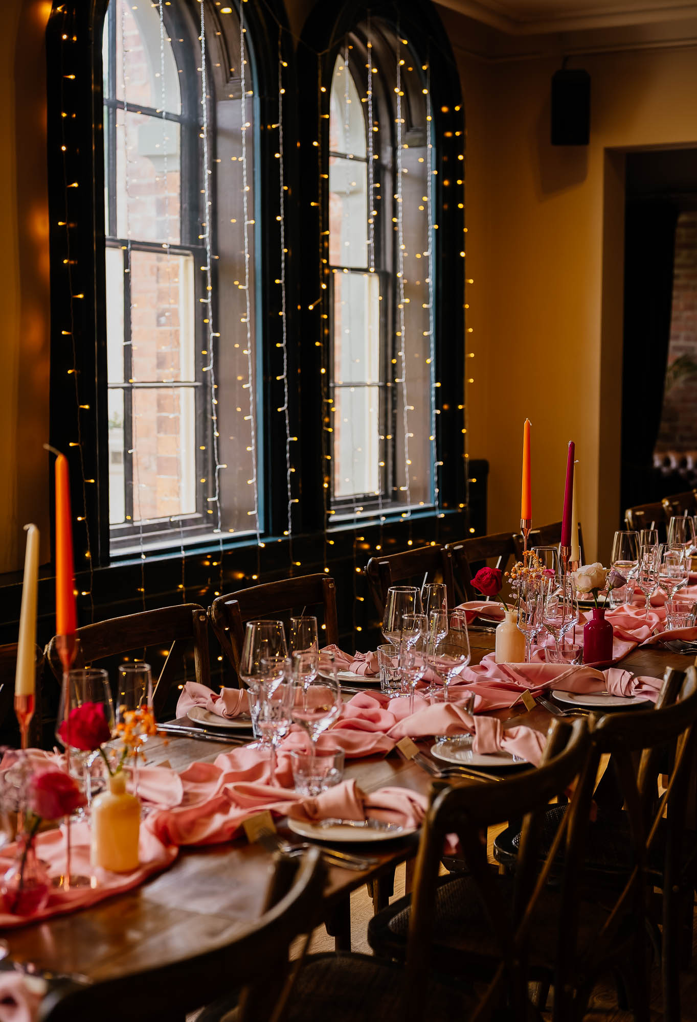 Long table set up for The Faversham wedding dinner under windows with fairy lights