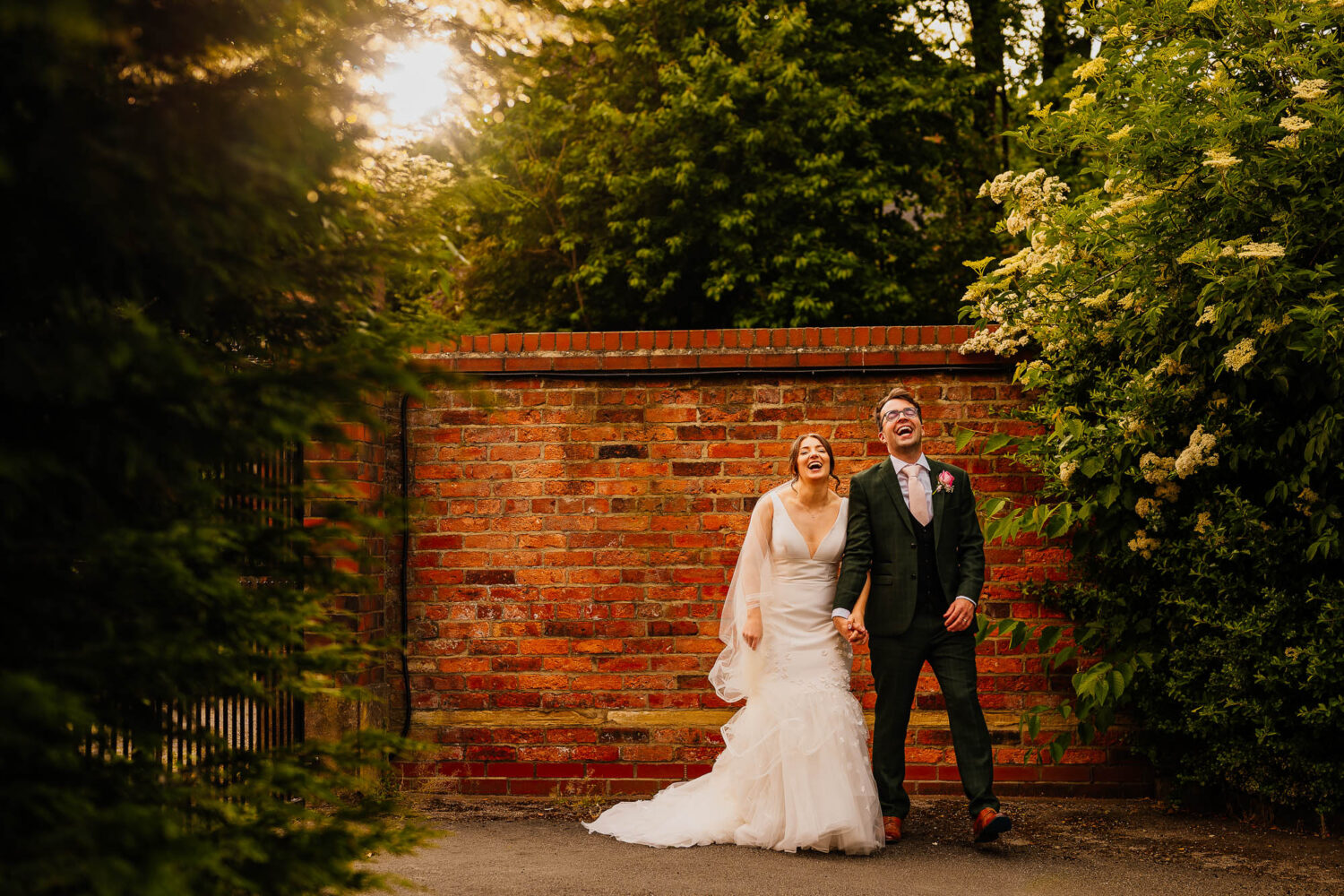 Couple holding hands and laughing against a brick wall at sunset