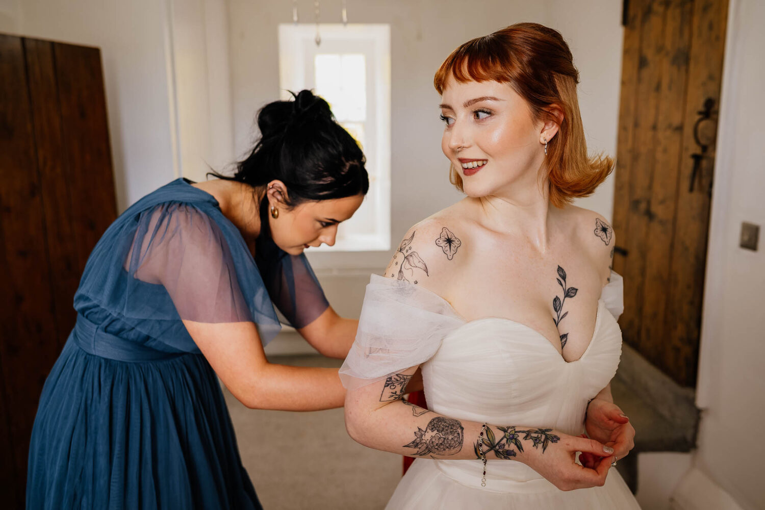 Bridesmaid tying dress whilst bride looks over her shoulder