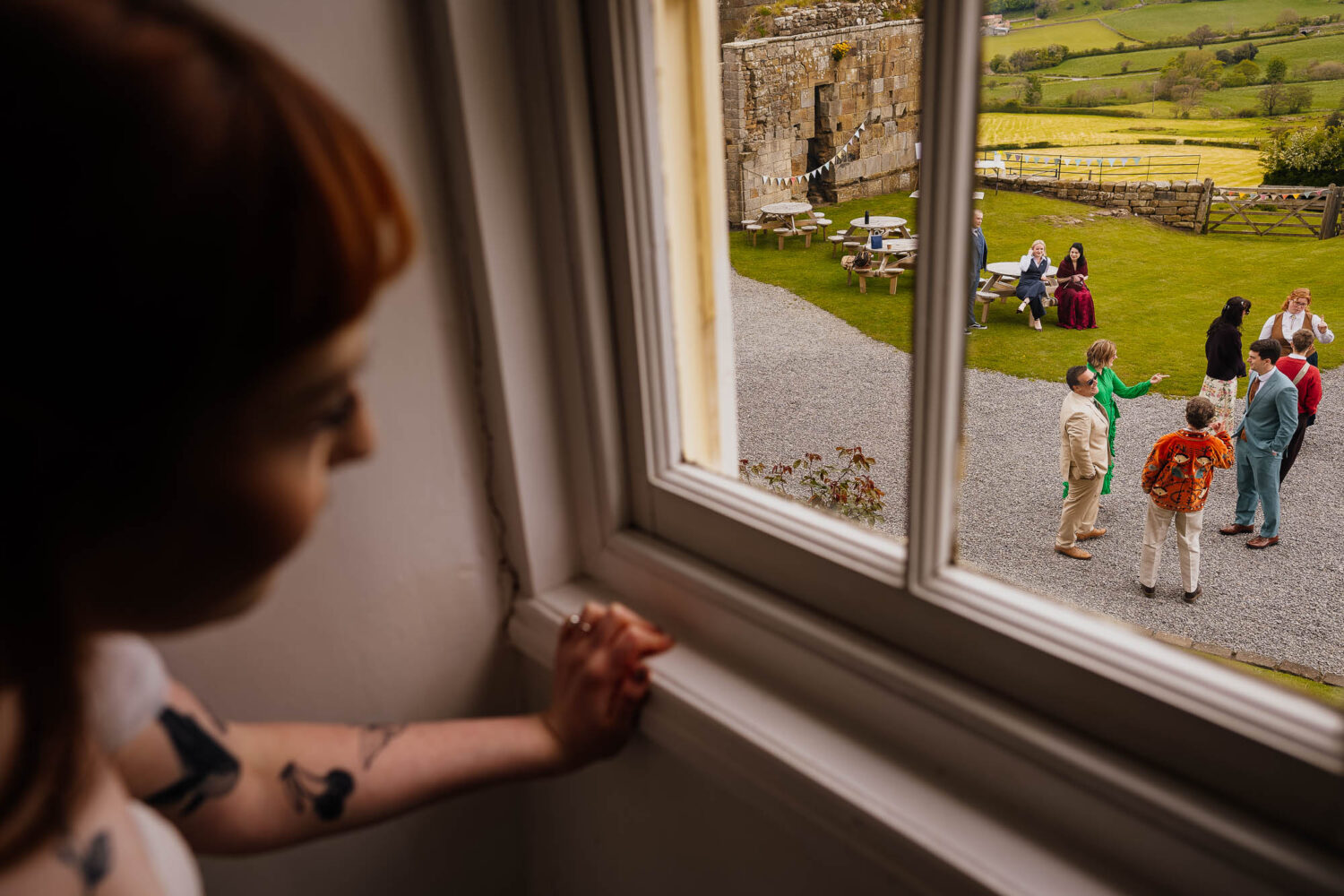 Bride peering out of the window to see groom and guests outside