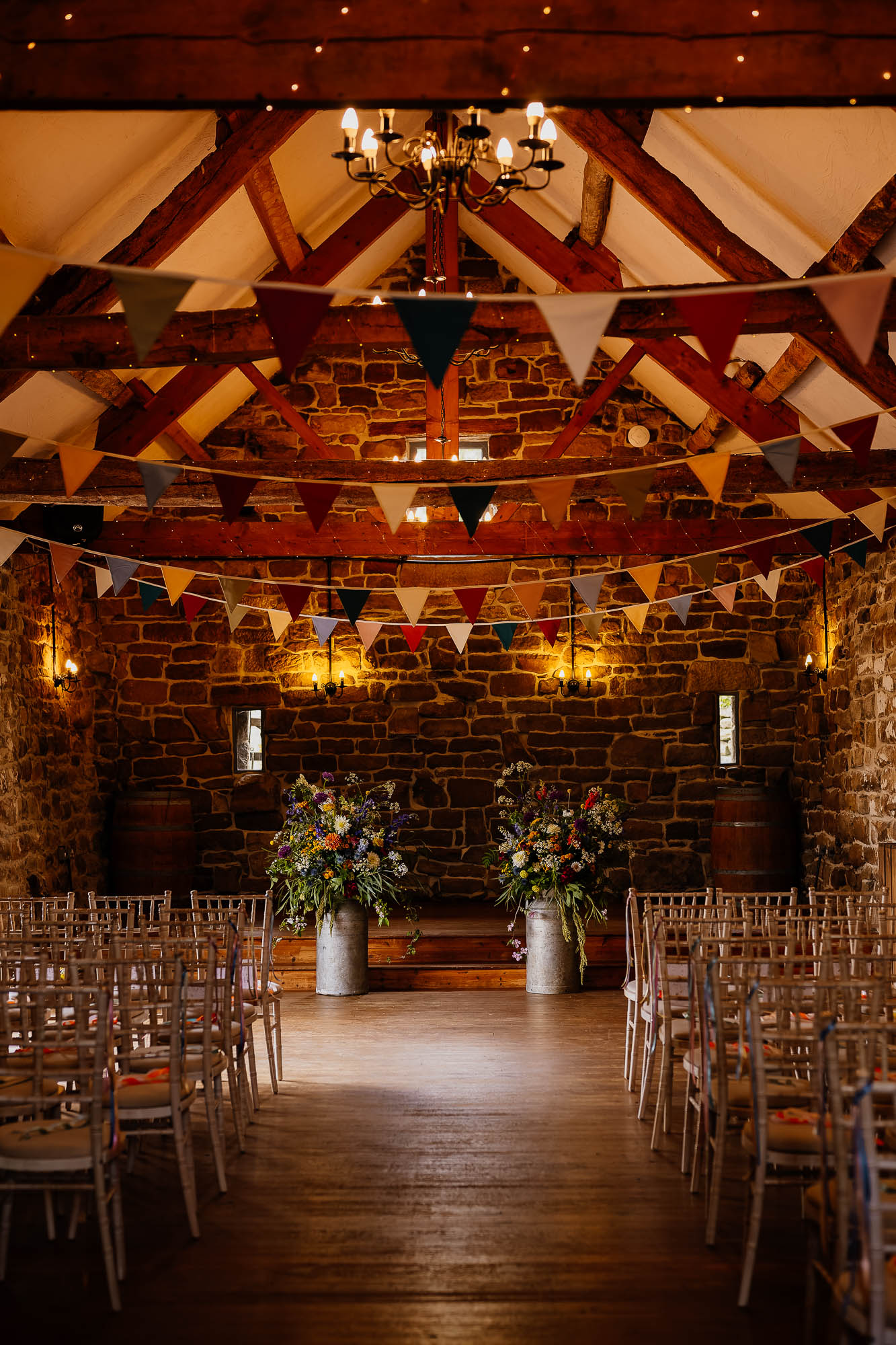 The barn at Danby castle set up for a ceremony with chairs, bunting and milk jugs full of flowers