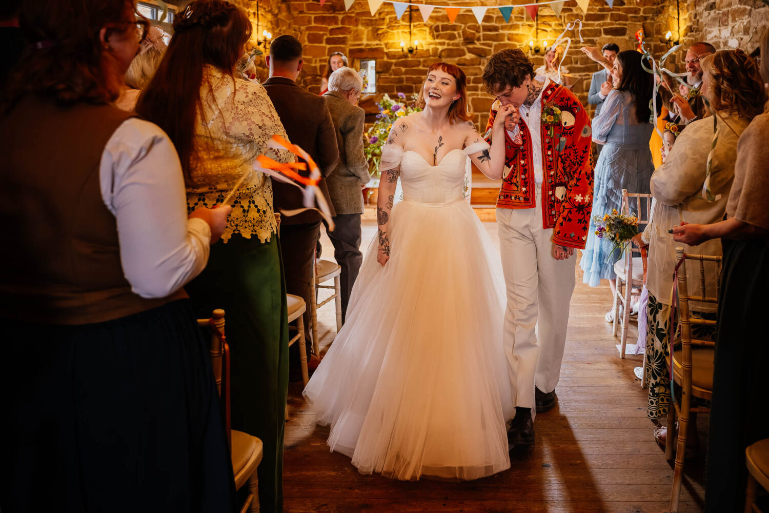 Groom kissing bride on hand during aisle exit at Danby Castle