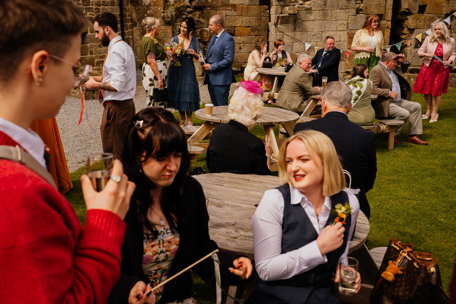 Wedding guests gathered around benches with drinks chatting
