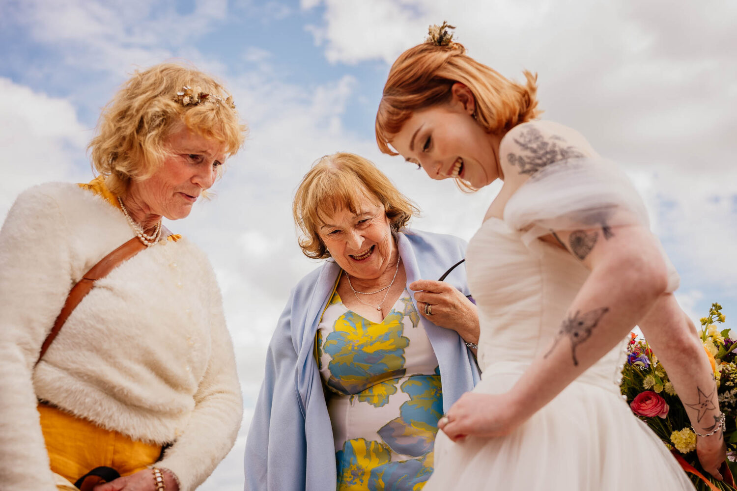 Guests smiling at bride's dress against a blue sky