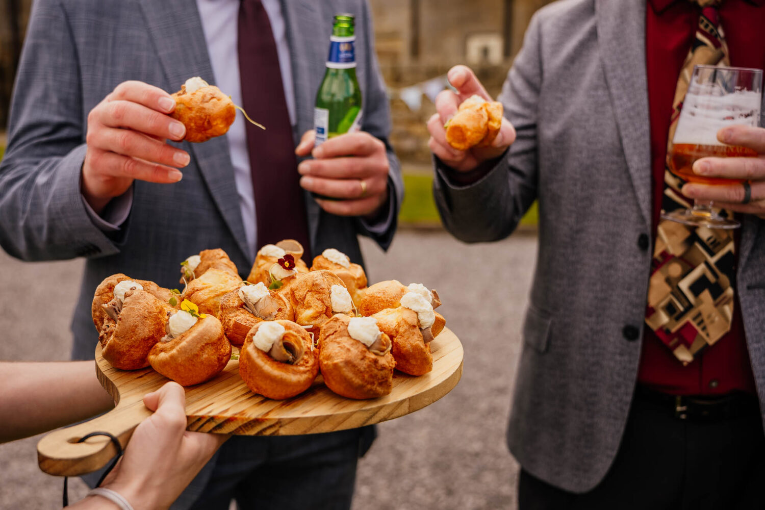 Board of Yorkshire pudding canapes being held out by staff with guests holding one in the background