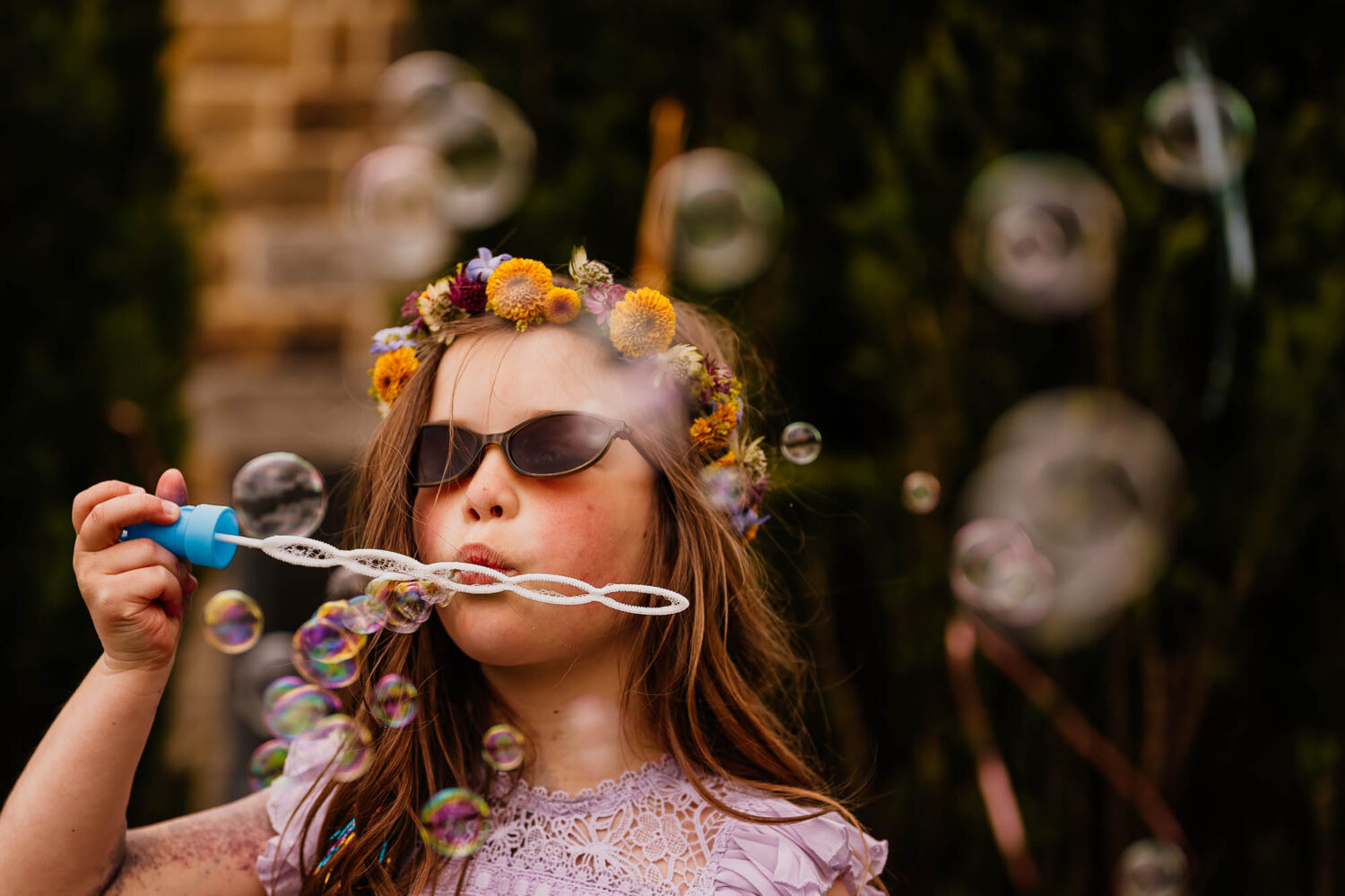 Girl with flower crown on blowing bubbles with sunglasses on