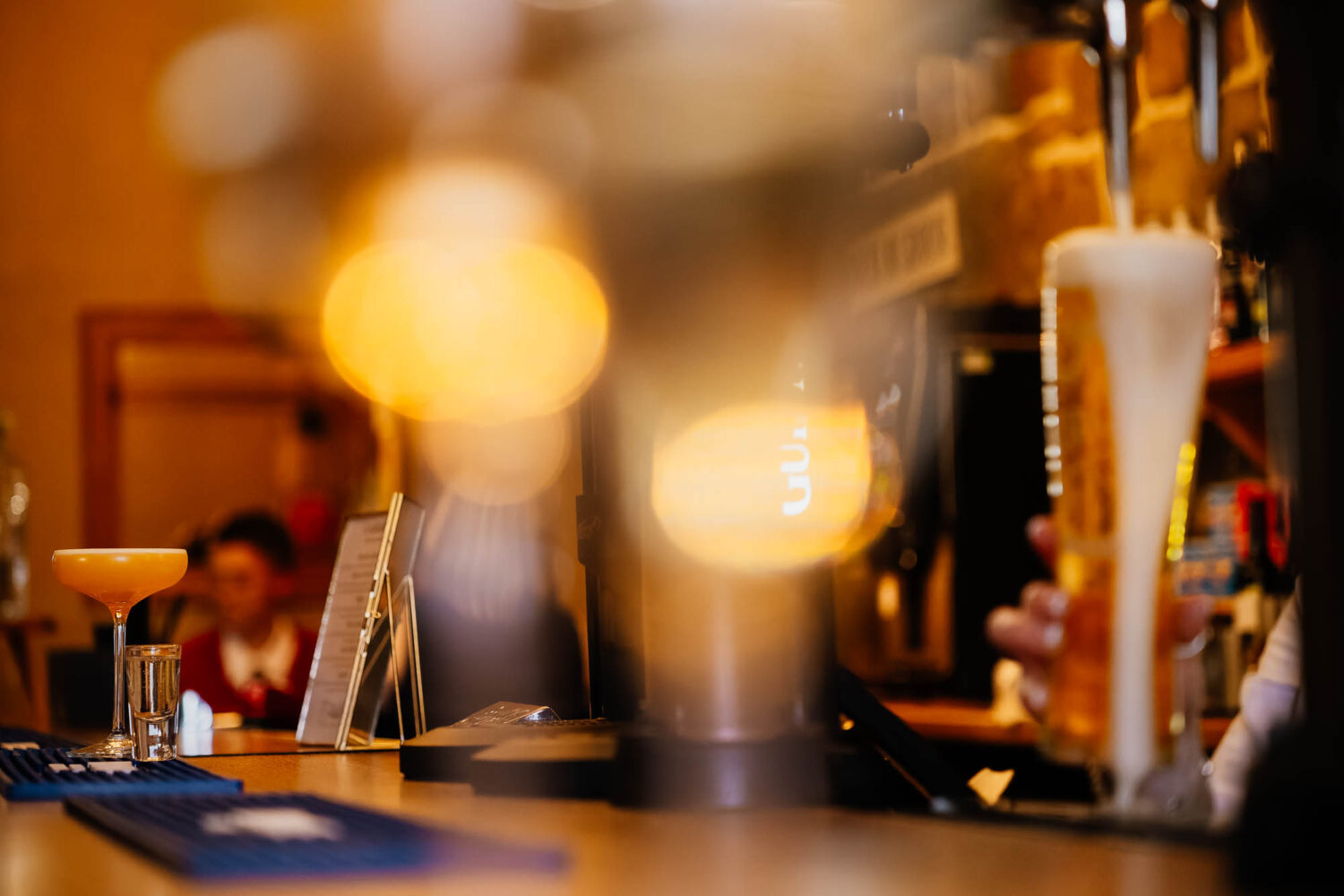 Cocktail sat on bar with pint of beer being poured
