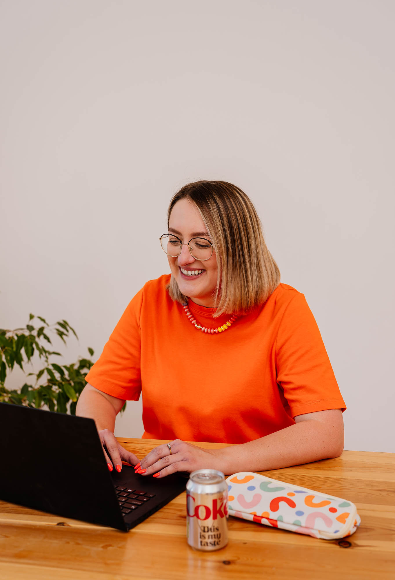 Woman smiling whilst working at her laptop on a wooden desk