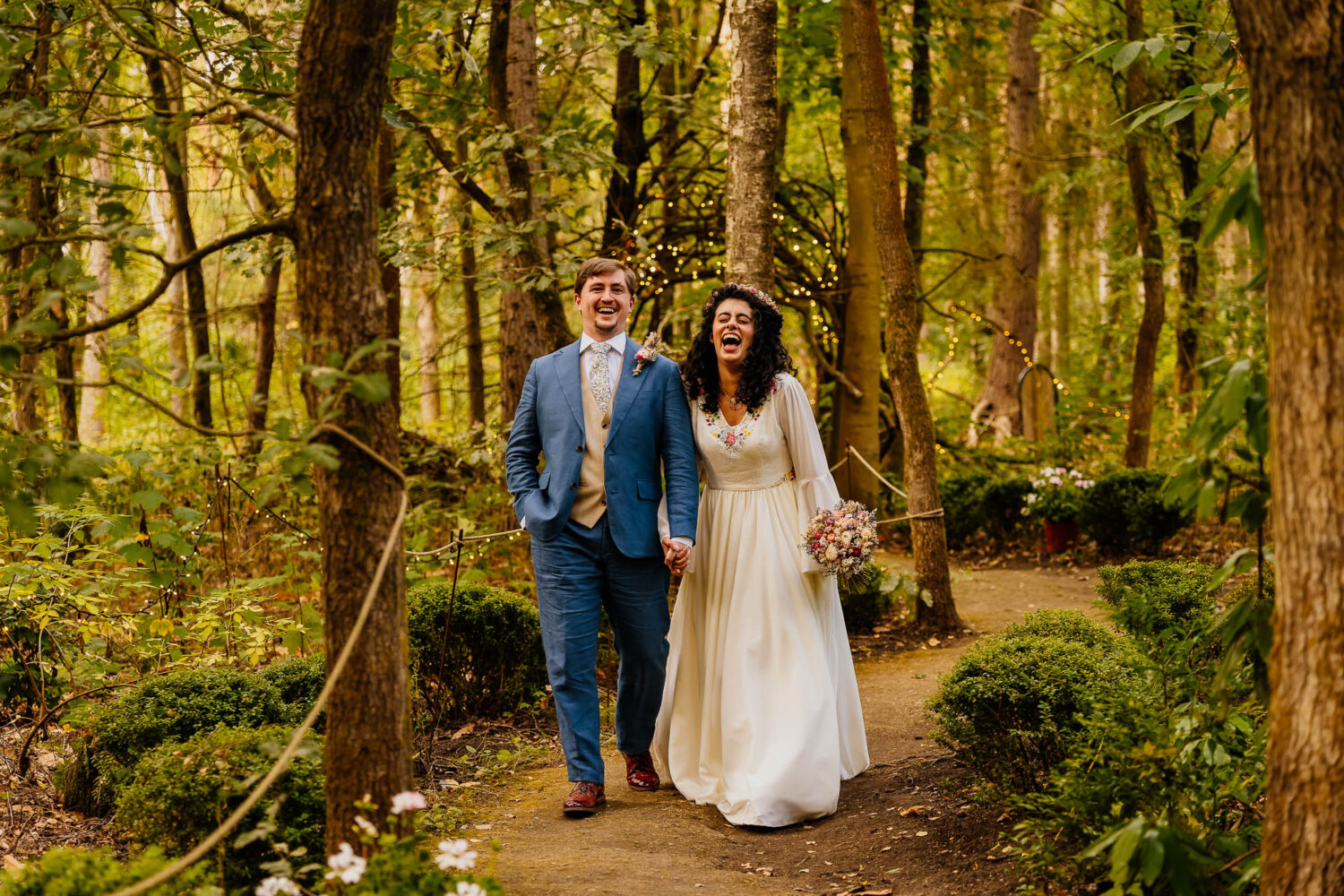 Couple holding hands walking through woodland trail at Dreamery Gardens laughing