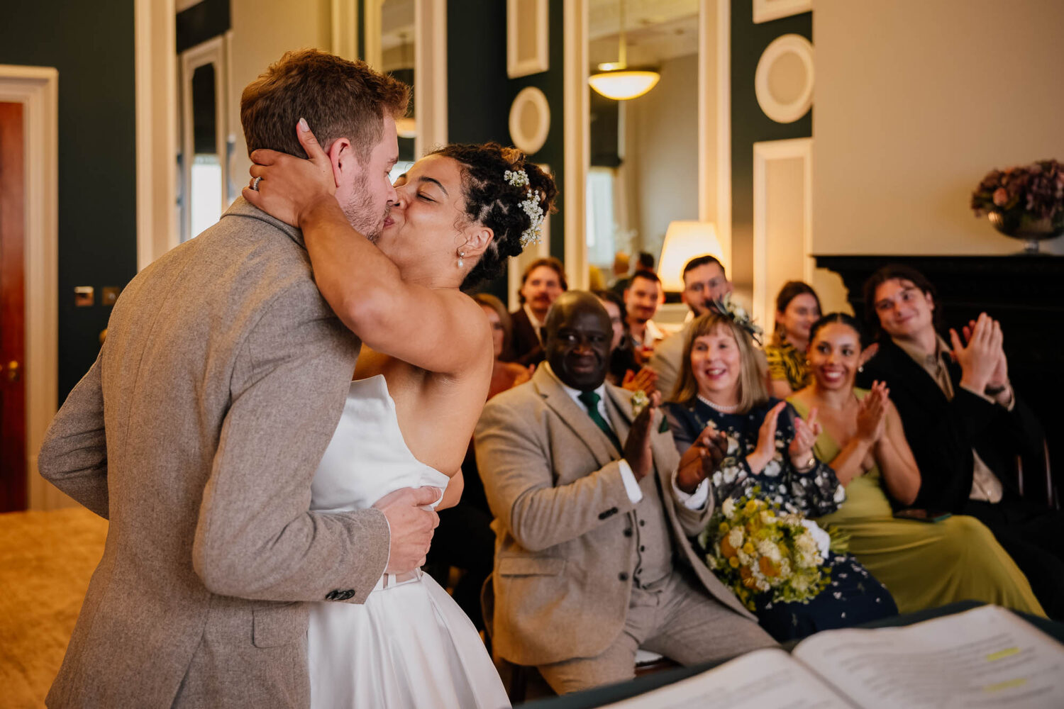 First kiss at Huddersfield Town Hall wedding with guests clapping behind