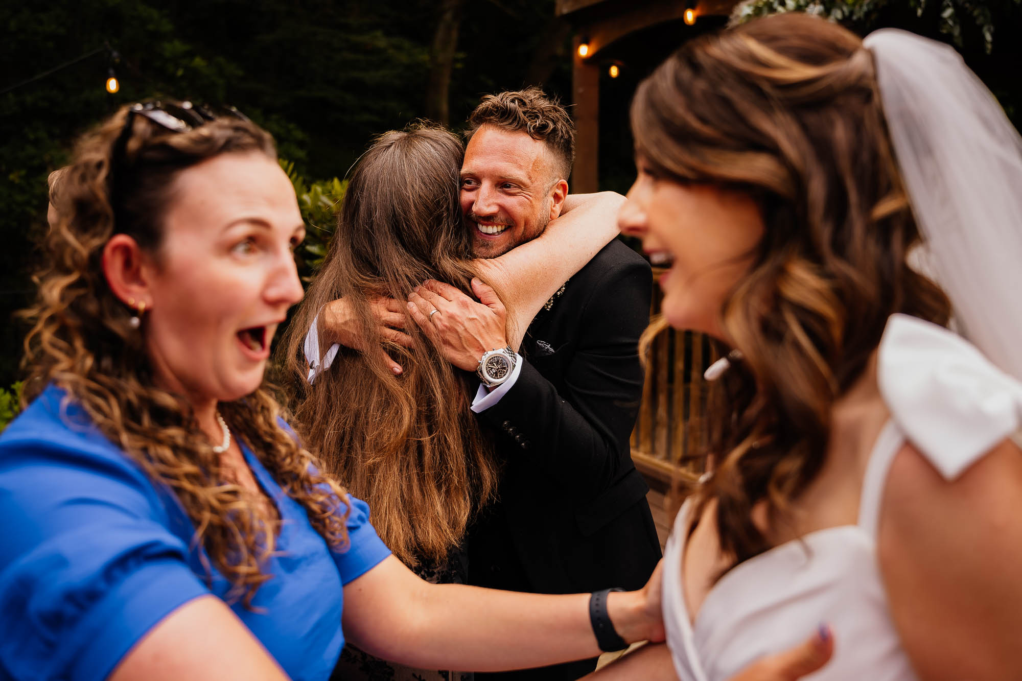 Groom hugging guest whilst another guest exclaims at the bride