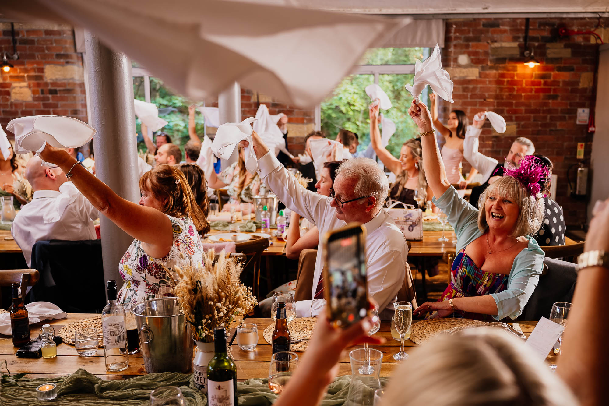 Wedding guests sat in Spinning Room at The Venue Bowers Mill waving napkins over their heads
