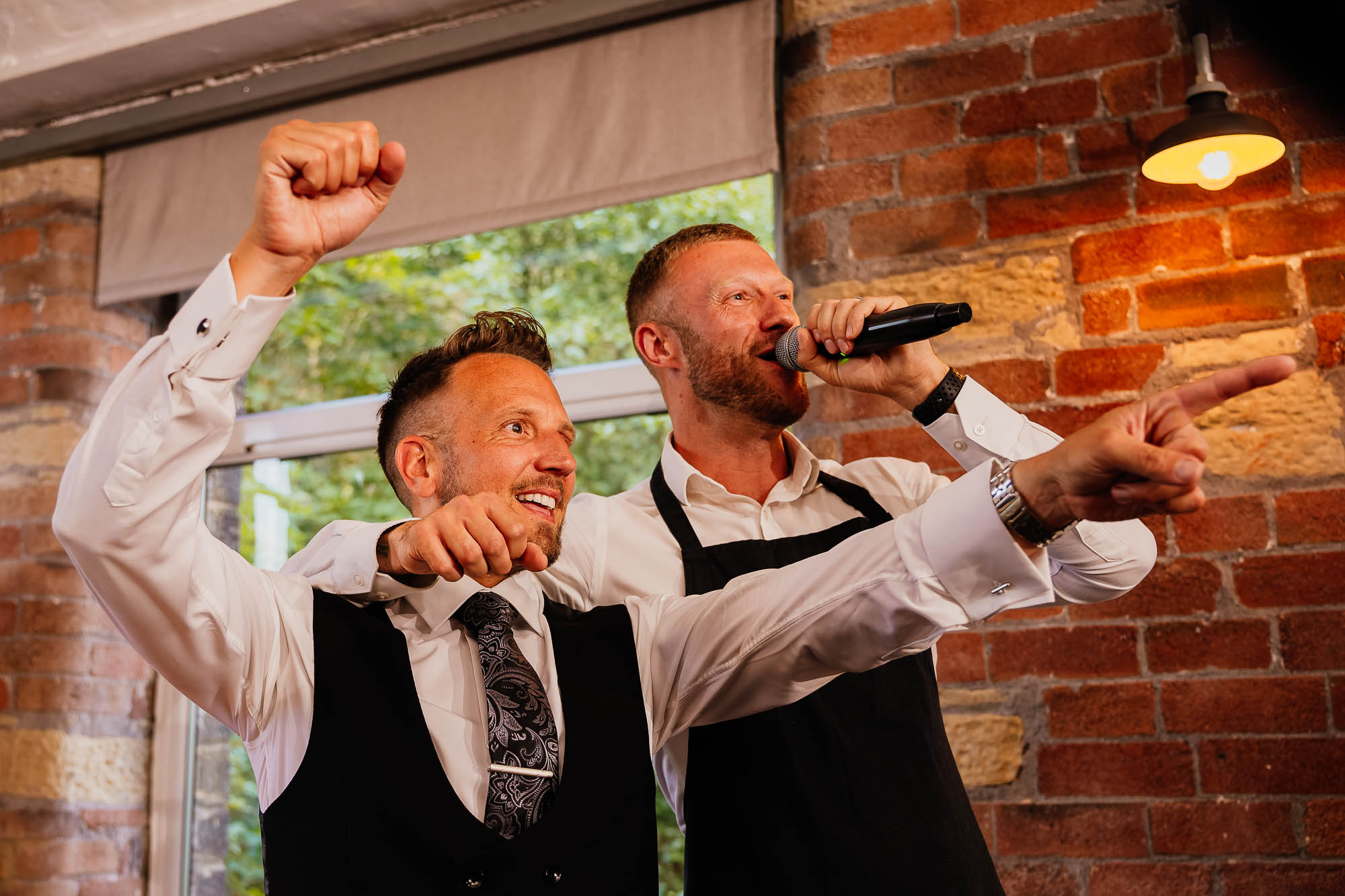 Groom cheering with singing waiter over his shoulder