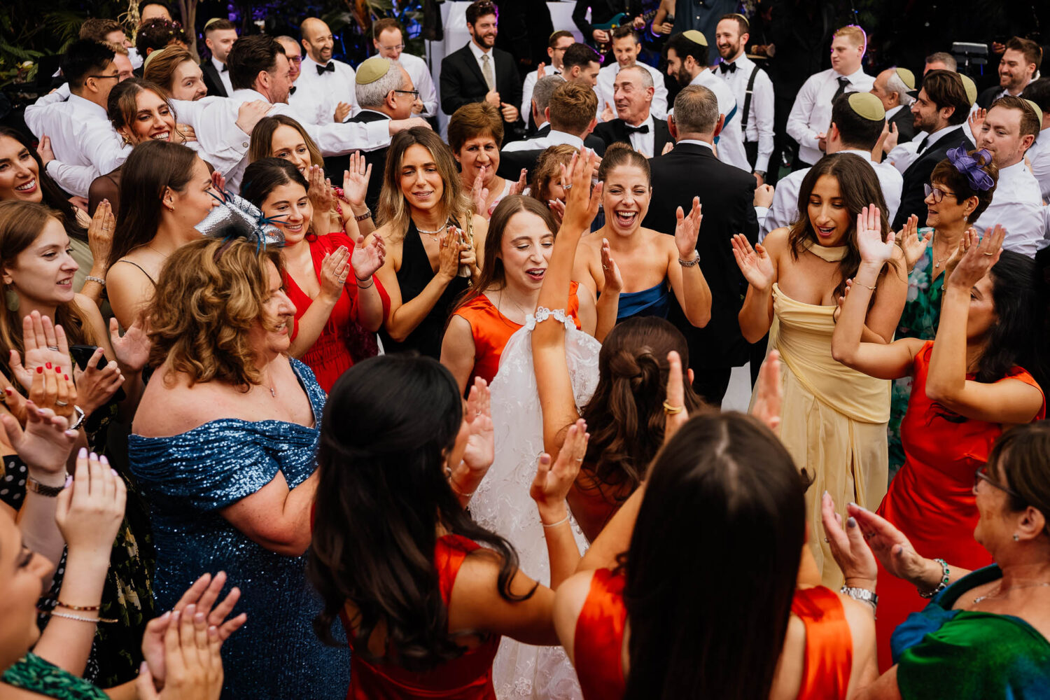 Happy wedding guests clapping and dancing around the bride at a lively jewish wedding reception celebration.